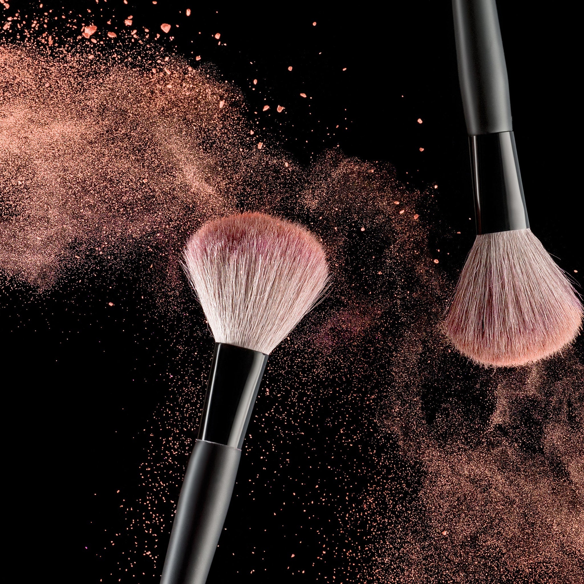 Makeup brushes with black handles and pink bristles in use with powder
