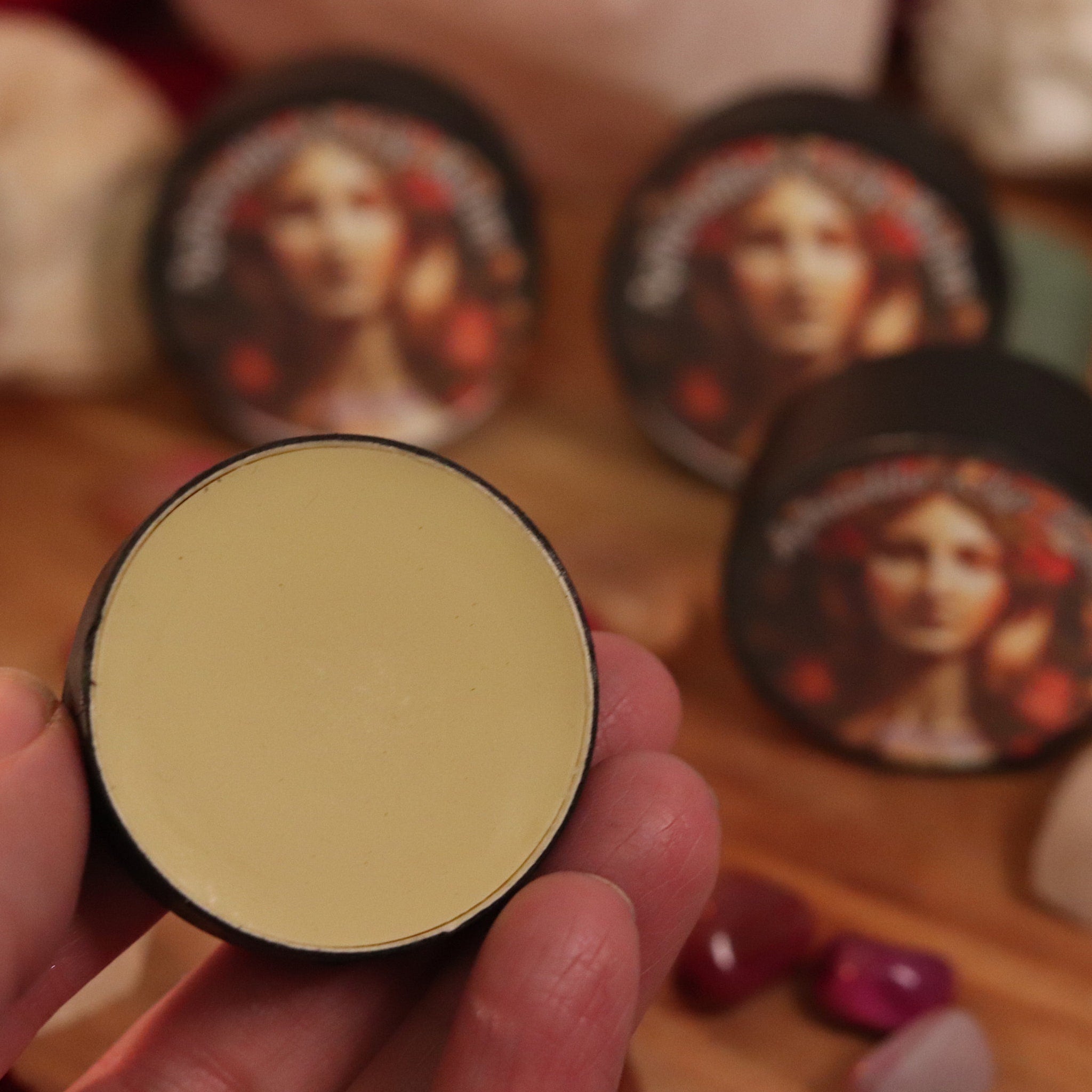 Cosmetic jar with yellow cream and black rim, held in hand, with other jars in background