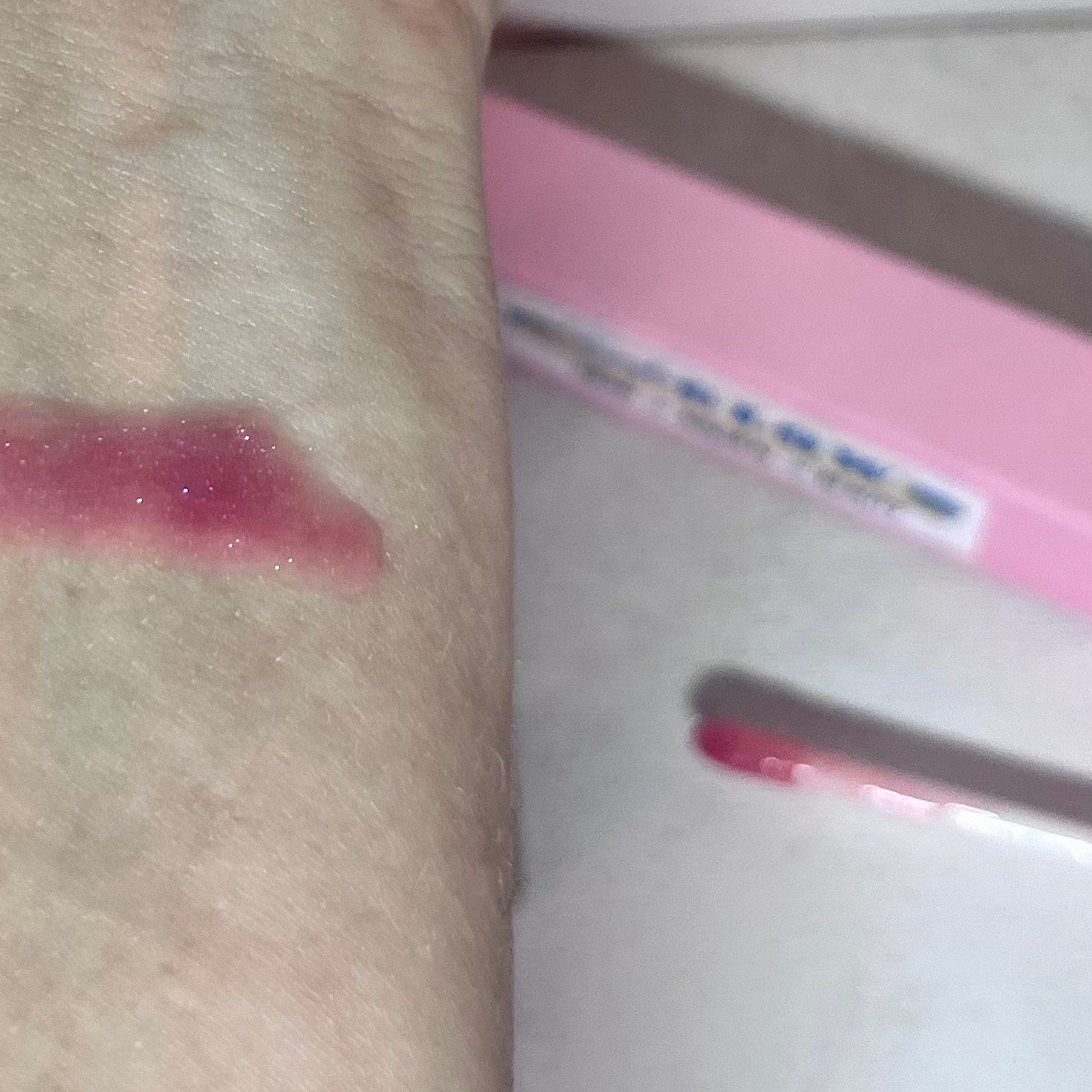 Lip gloss swatch with pink and glitter on skin, showing color test application