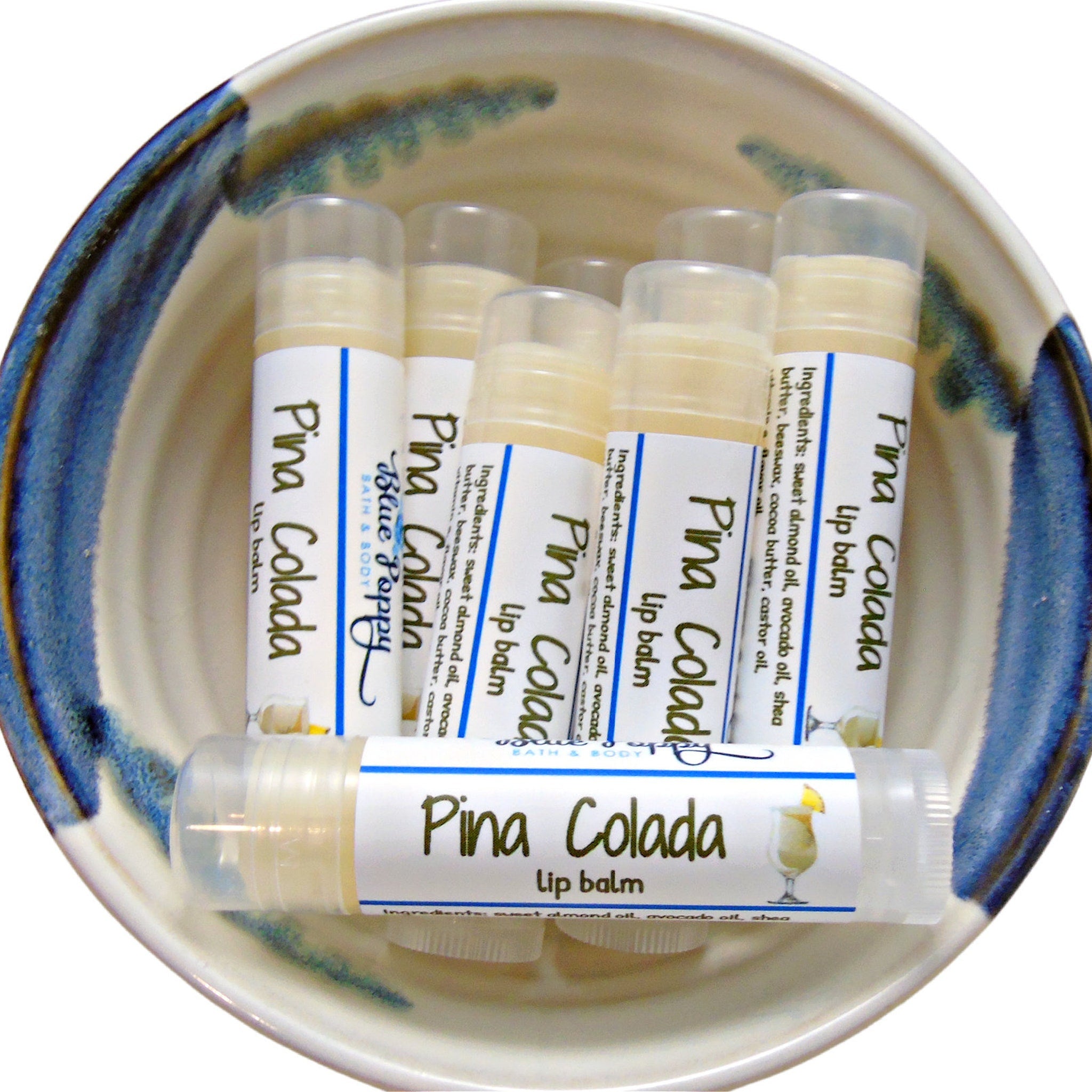 Lip balm tubes with white labels, clear caps, and "Pina Colada" text in a ceramic bowl