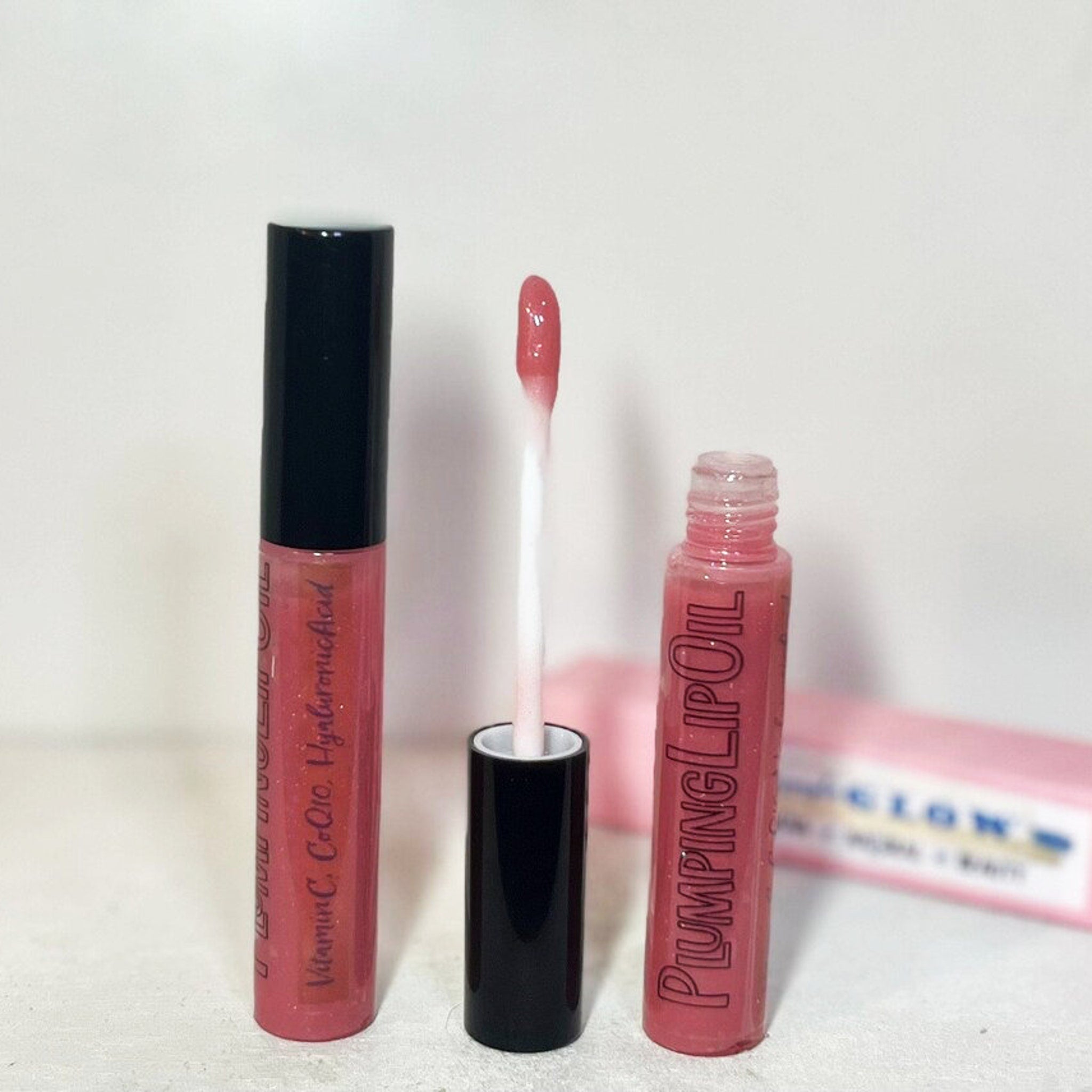 Lip gloss tubes with pink gloss, black caps, and white applicator wand, PLUMPING LIP OIL text