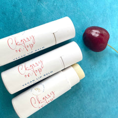 Lip balm tubes with white paper, red script text, and cherry on blue background