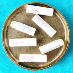Lip balm tubes in white with pink text, on gold tray, some open showing product