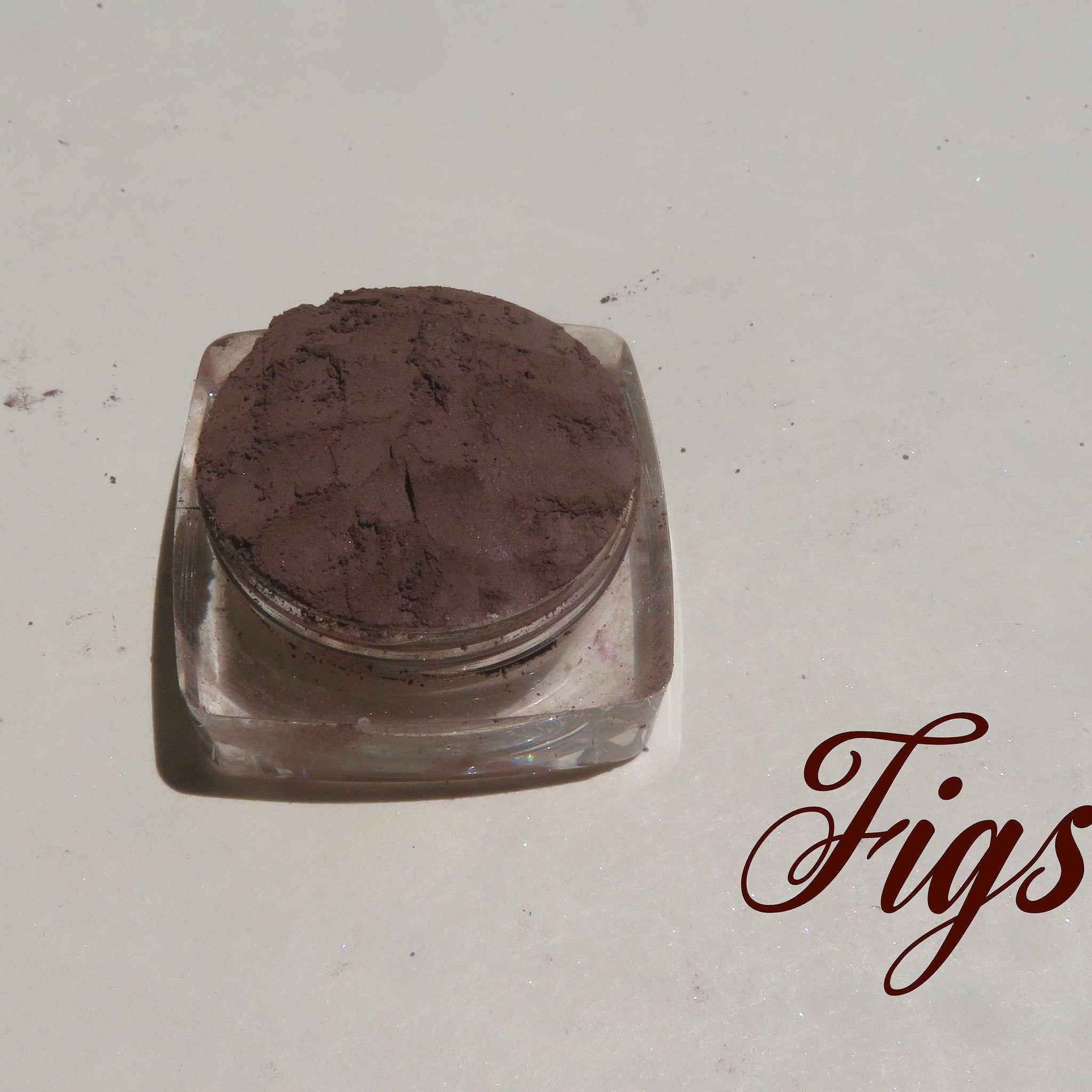 Side view of dark brown matte mineral eye shadow in loose powder form with vegan labeling on container