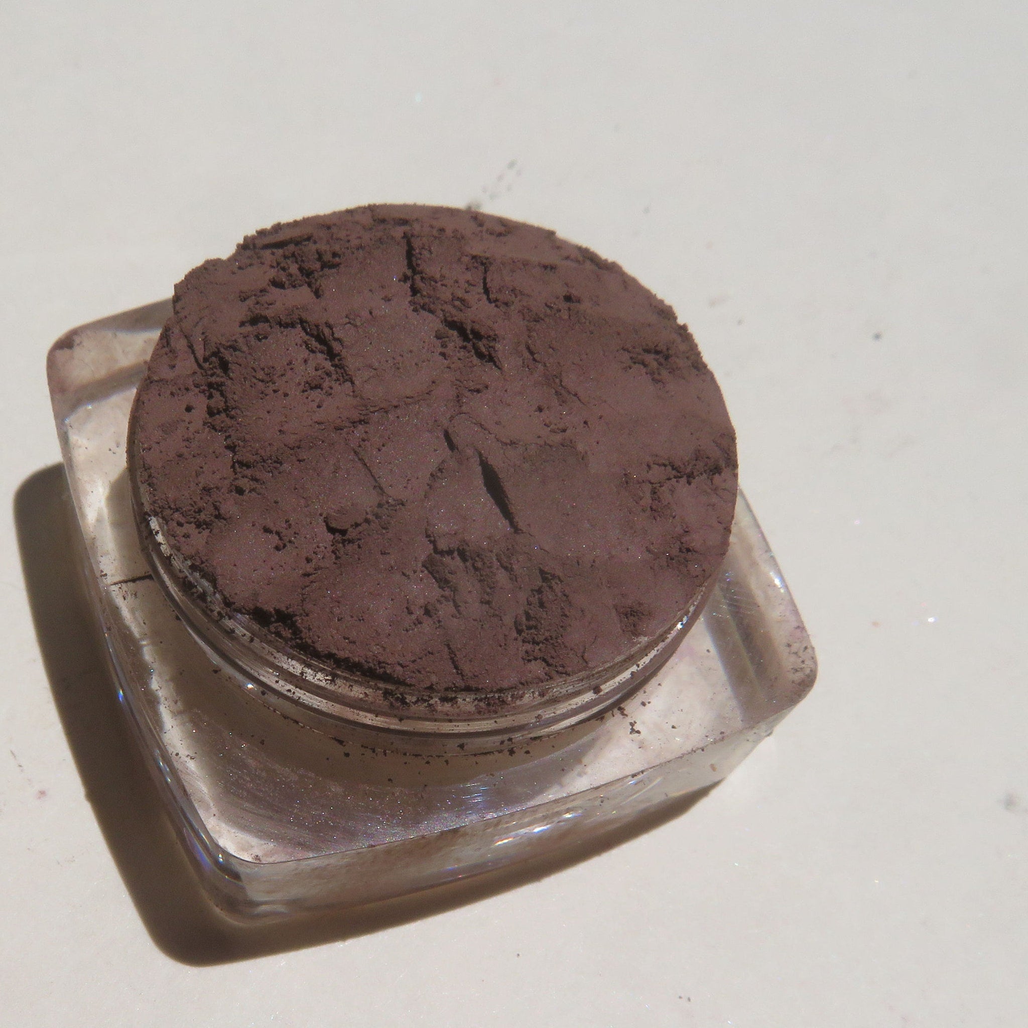 Open compact showing loose dark brown matte mineral eyeshadow with vegan label on sleek black packaging