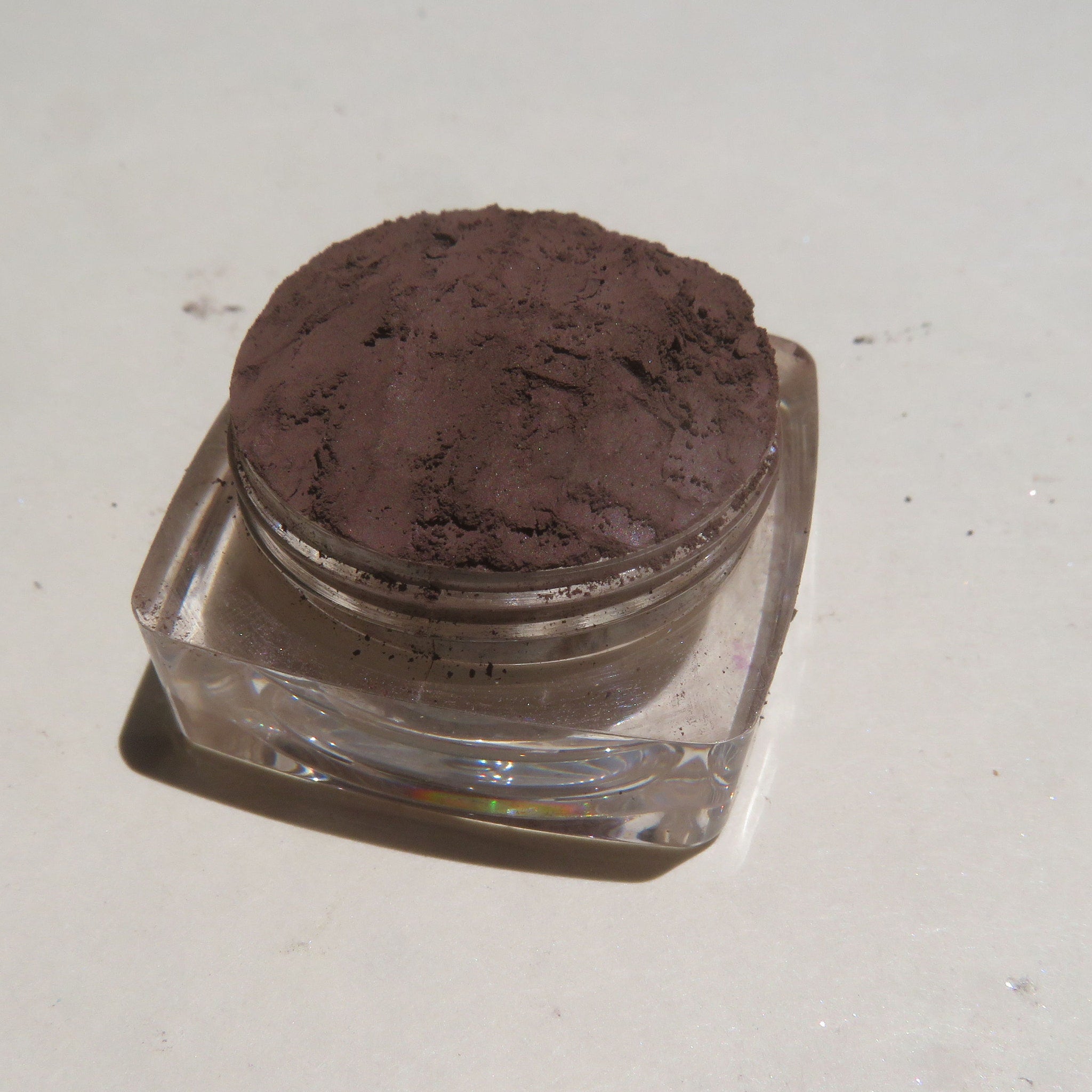 Close-up of loose dark brown matte mineral eye shadow powder with fine texture in a small open jar