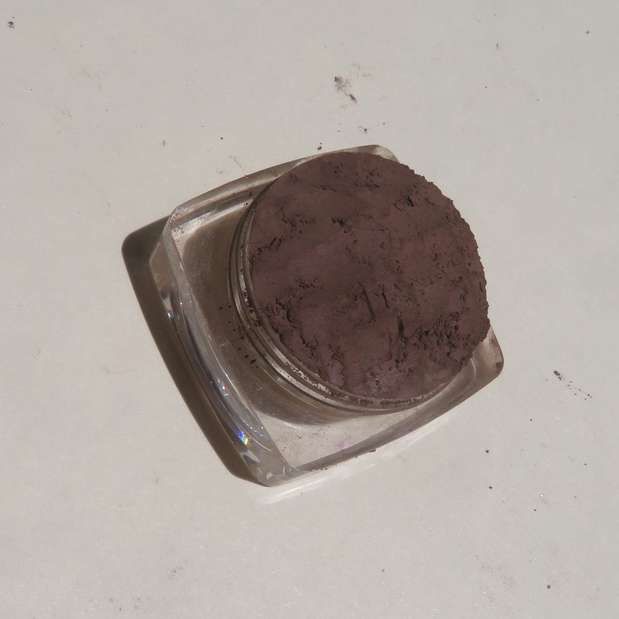 Side view of dark brown matte mineral eye shadow in loose powder form with vegan labeling visible