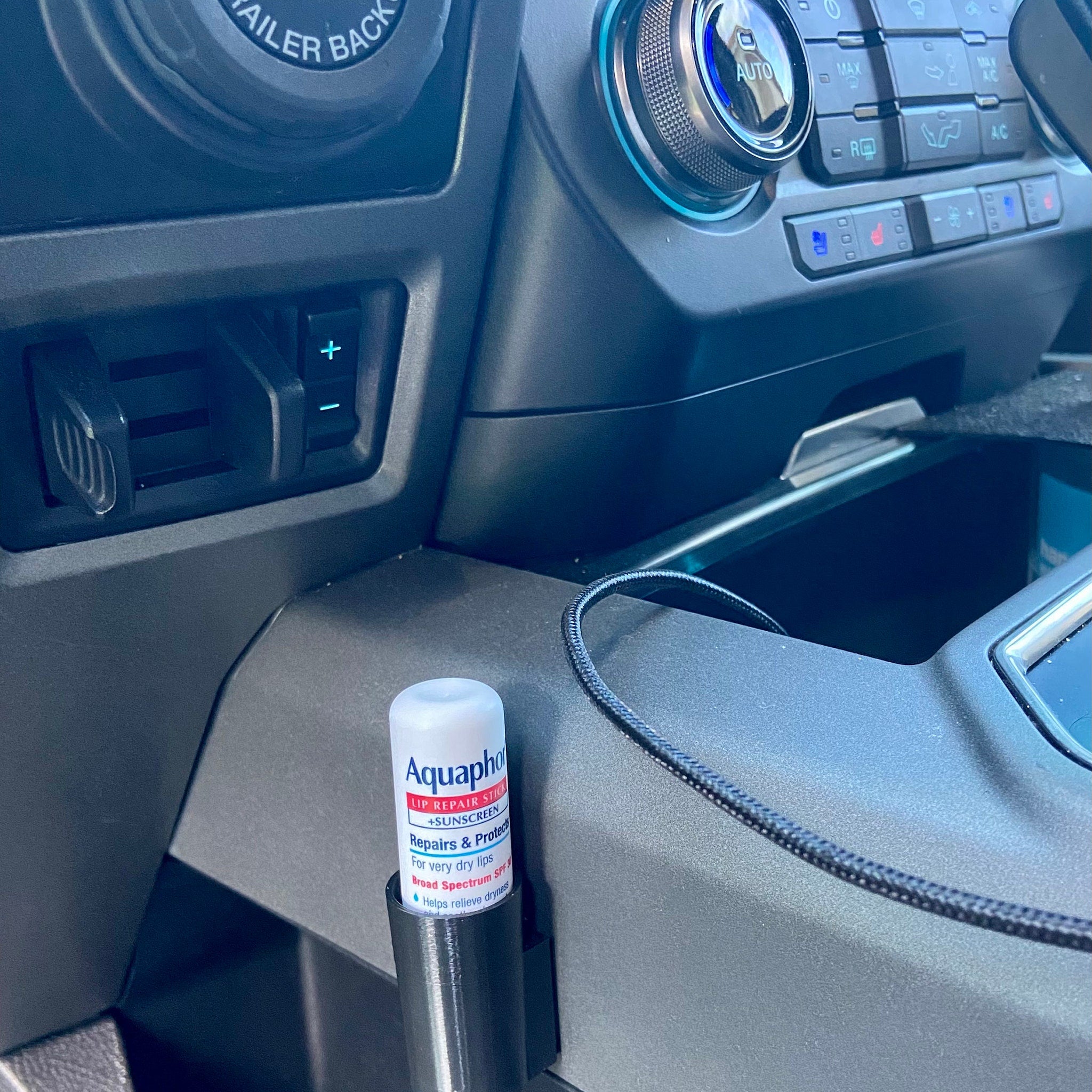 Lip balm tube with white and red label, black holder, and car interior background