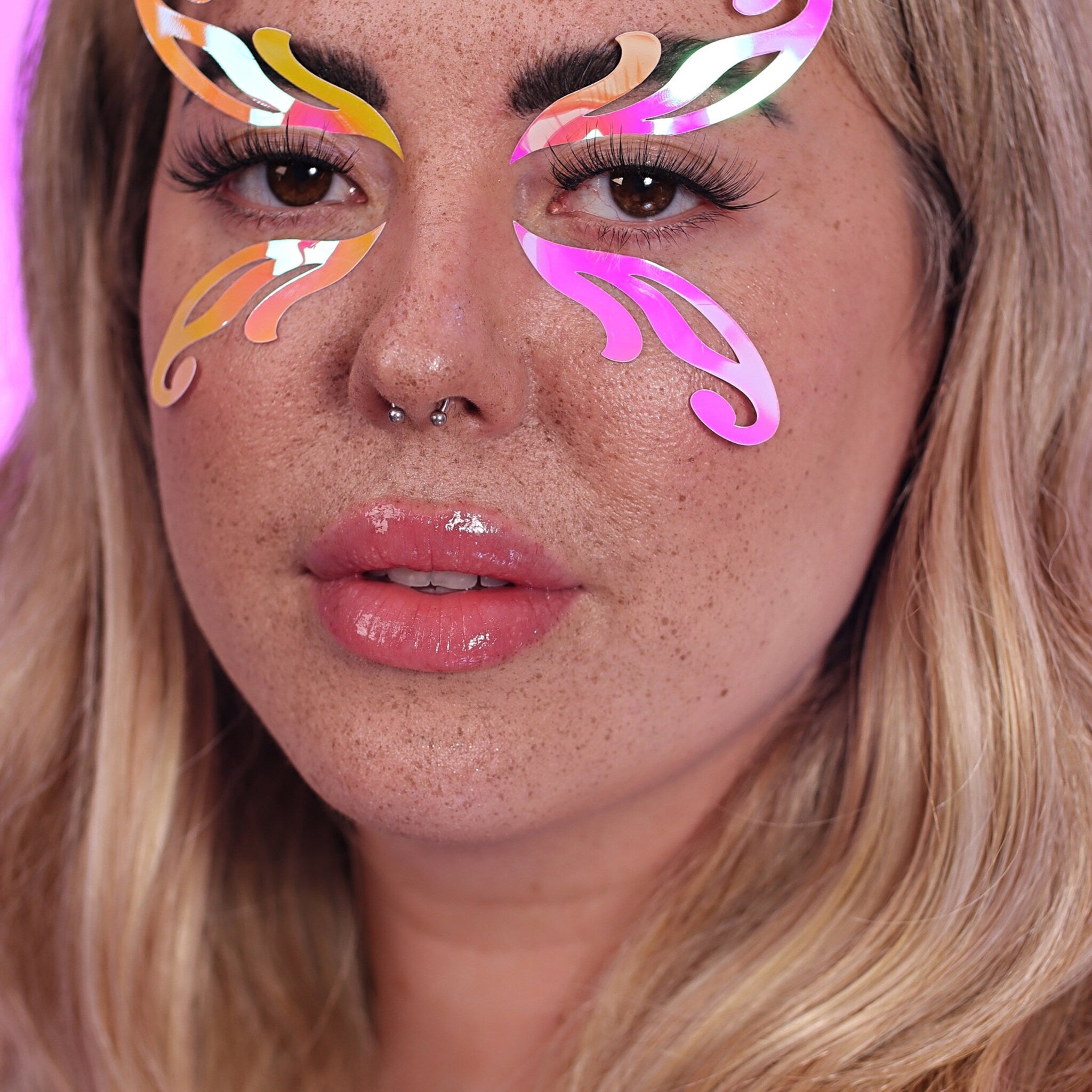Face stickers with iridescent and pink butterfly shapes over eyes, blonde hair, and freckled skin