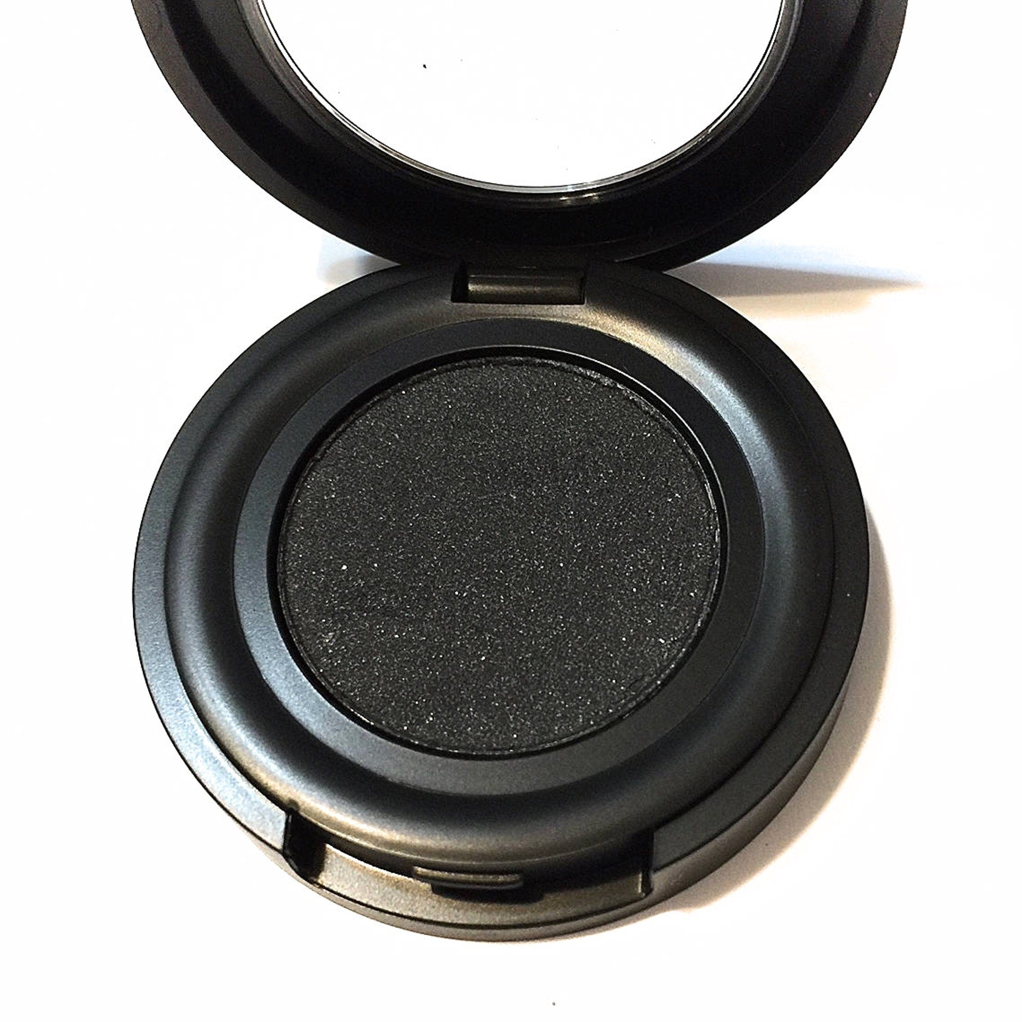 Side view of black pressed mineral eyeshadow pan showing smooth matte texture and compact case