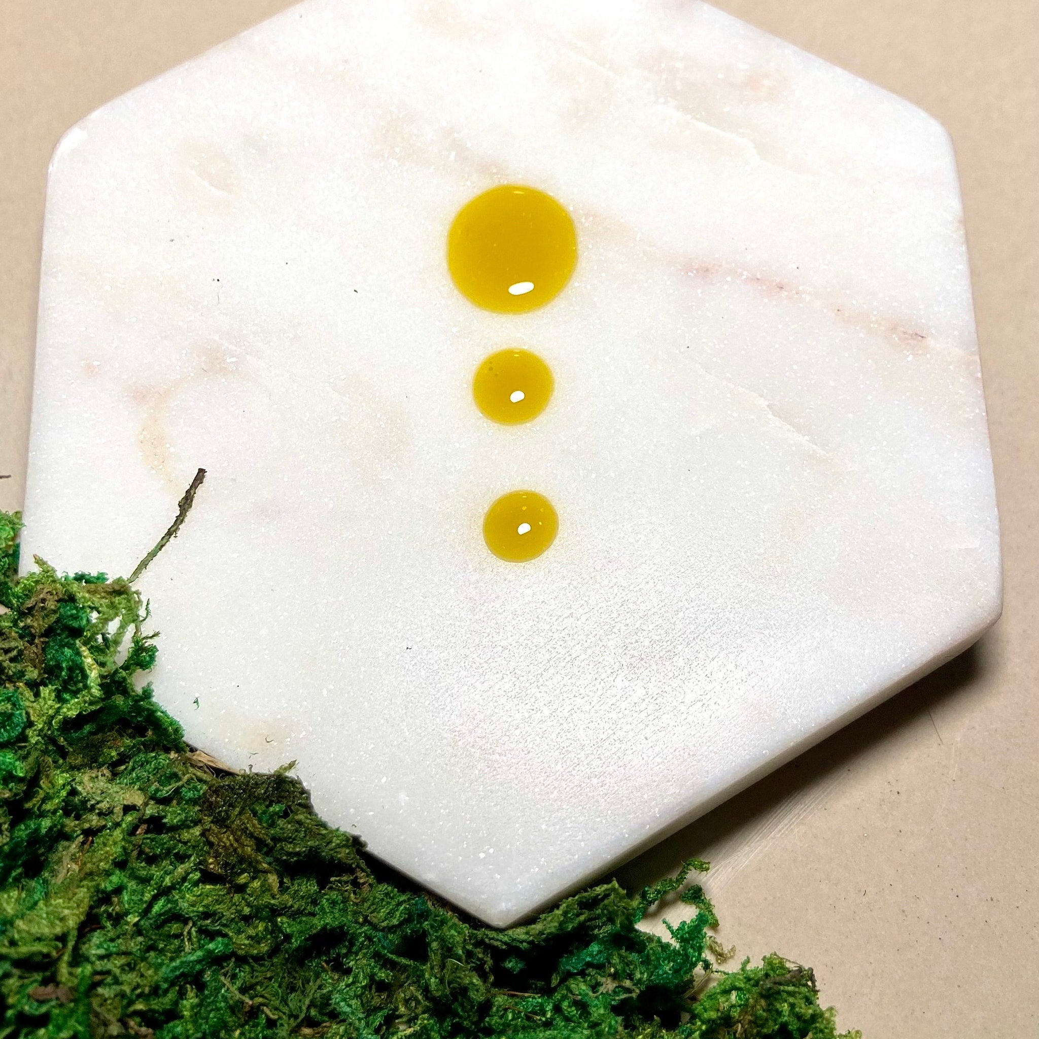 Yellow liquid drops on white marble hexagon with green moss