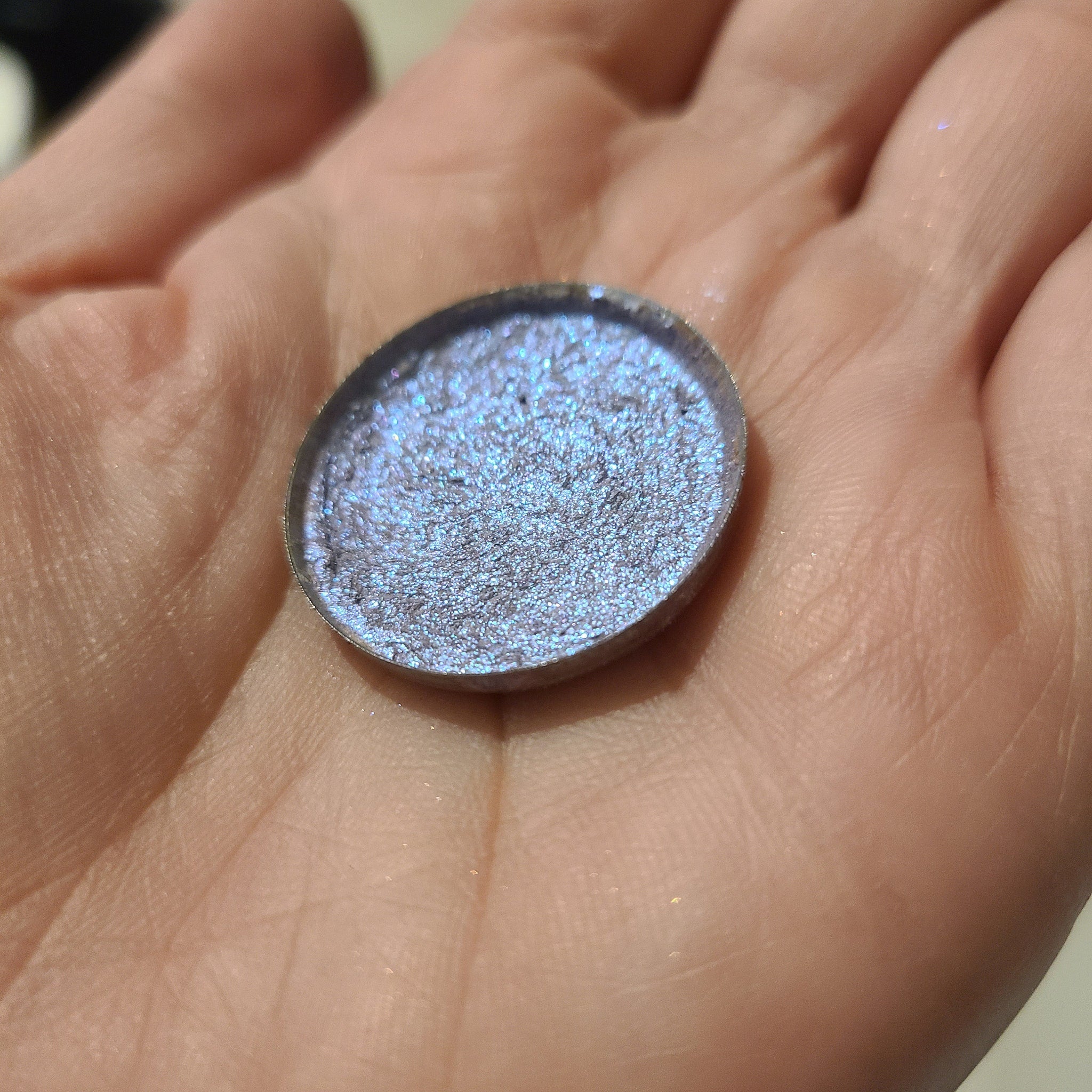Close-up of fingertips applying bright blue-shifting eye shadow with metallic sheen to eyelid