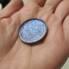 Close-up of fingertips applying bright blue-shifting eye shadow with metallic sheen to eyelid