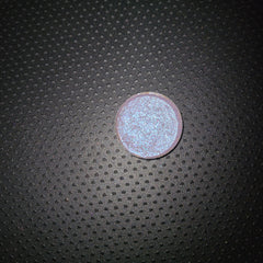 Side view of bright blue-shifting eye shadow pot catching light, showcasing iridescent shimmer and compact size