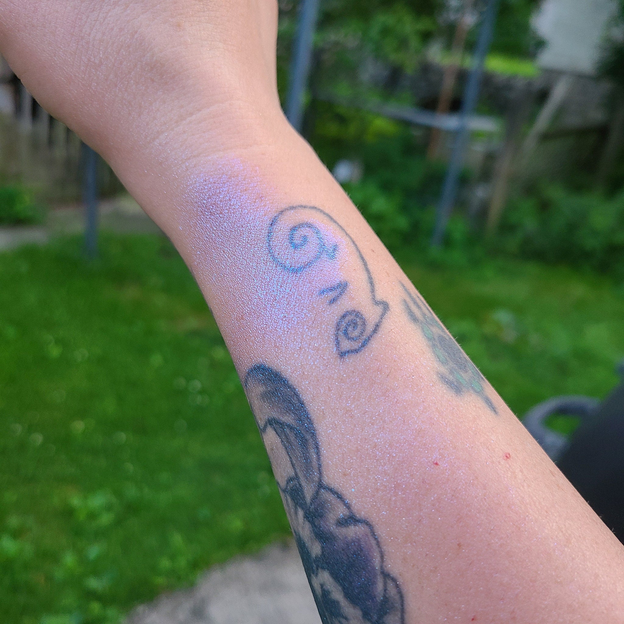 Side view of Black Lite Edit eye shadow pot showing bright blue-shifting pigment with reflective highlighter particles.