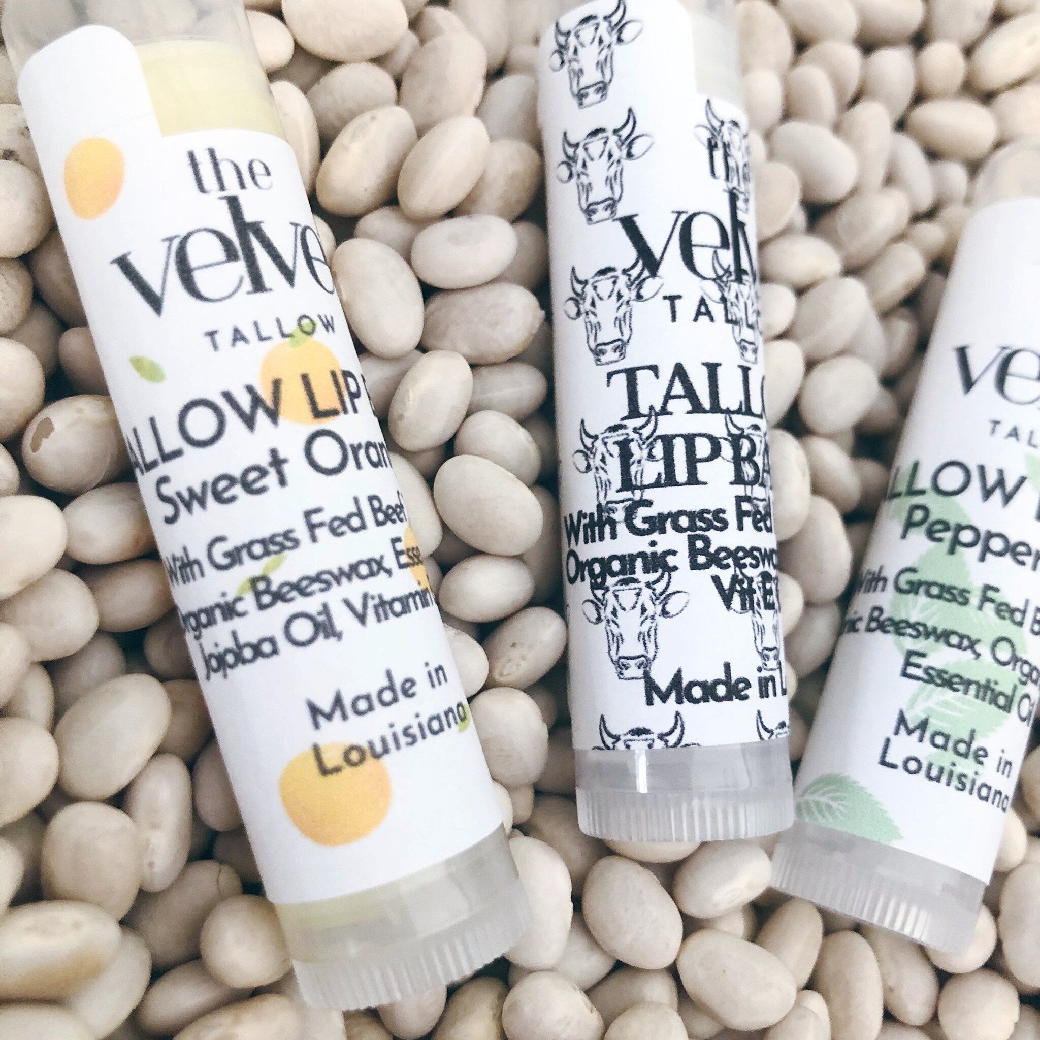 Lip balm tubes with white labels, black text, and cow illustrations on white beans background