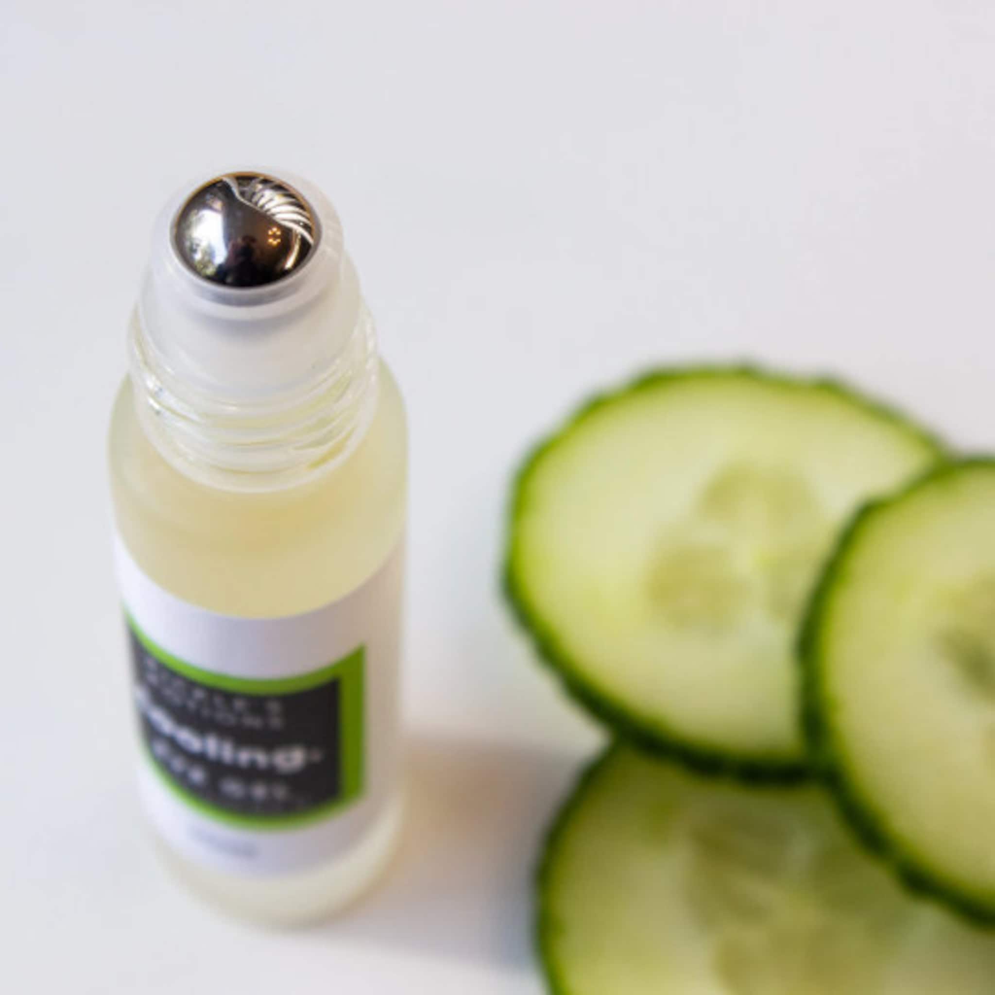 Eye oil bottle with clear glass, silver rollerball, and green label near cucumber slices