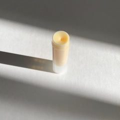Lip balm in clear plastic tube with pale yellow balm and white base, on white surface