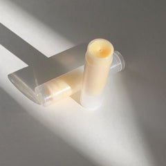 Vegan lip balm with light yellow balm, clear plastic tube, and white cap on white surface