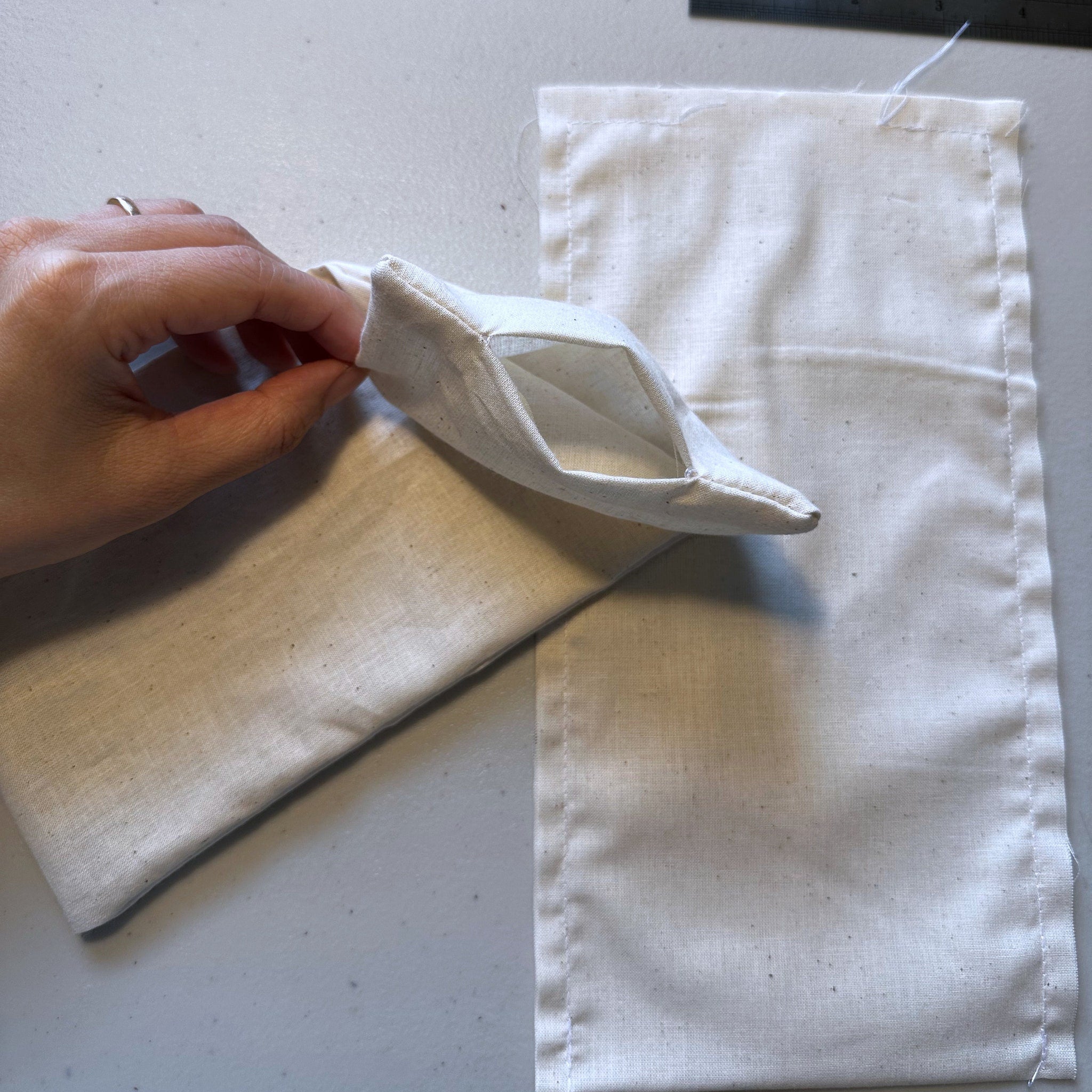 White fabric pouch with open pocket, beige material, hand holding open pouch