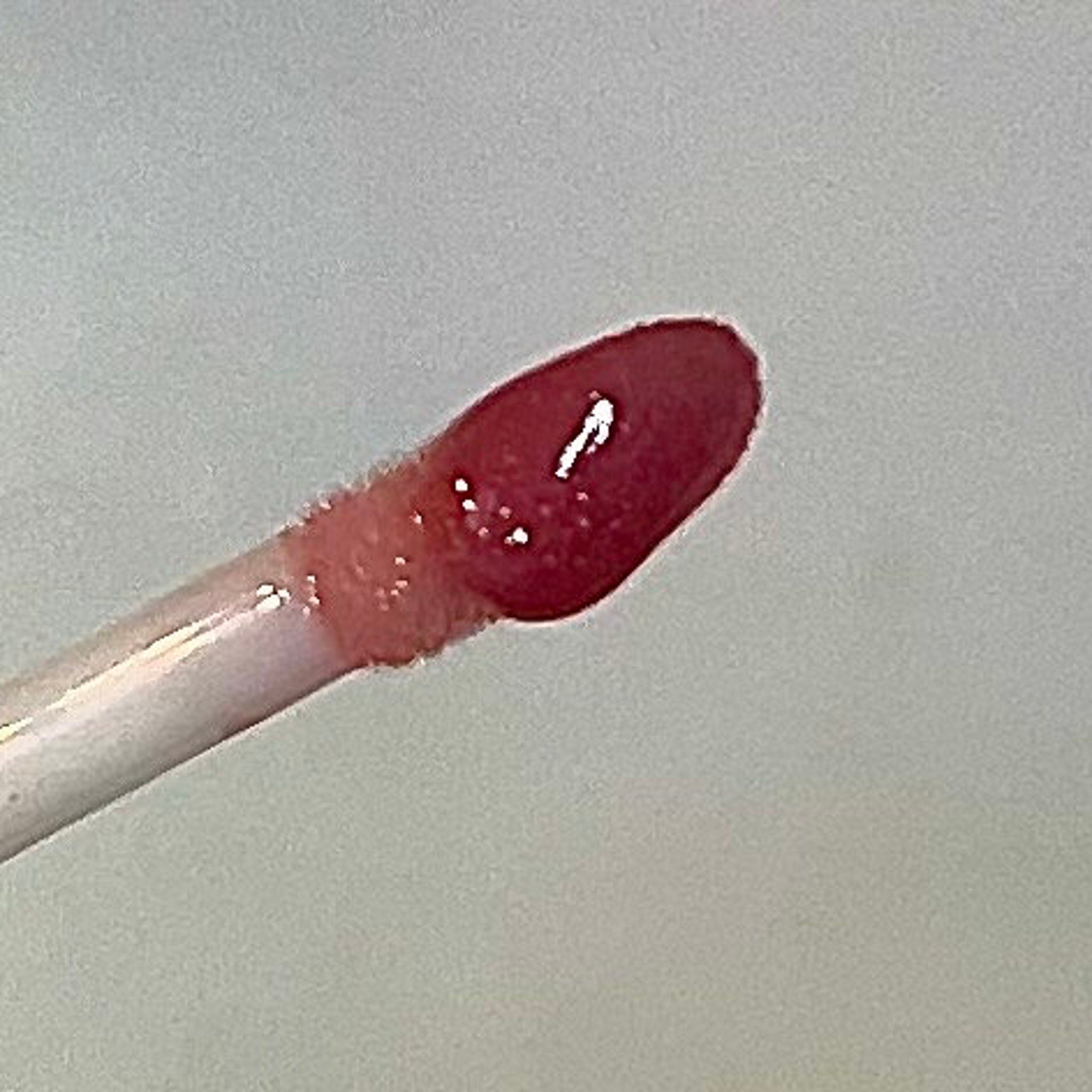 Lip gloss applicator with red-pink gloss, white wand, and glossy finish
