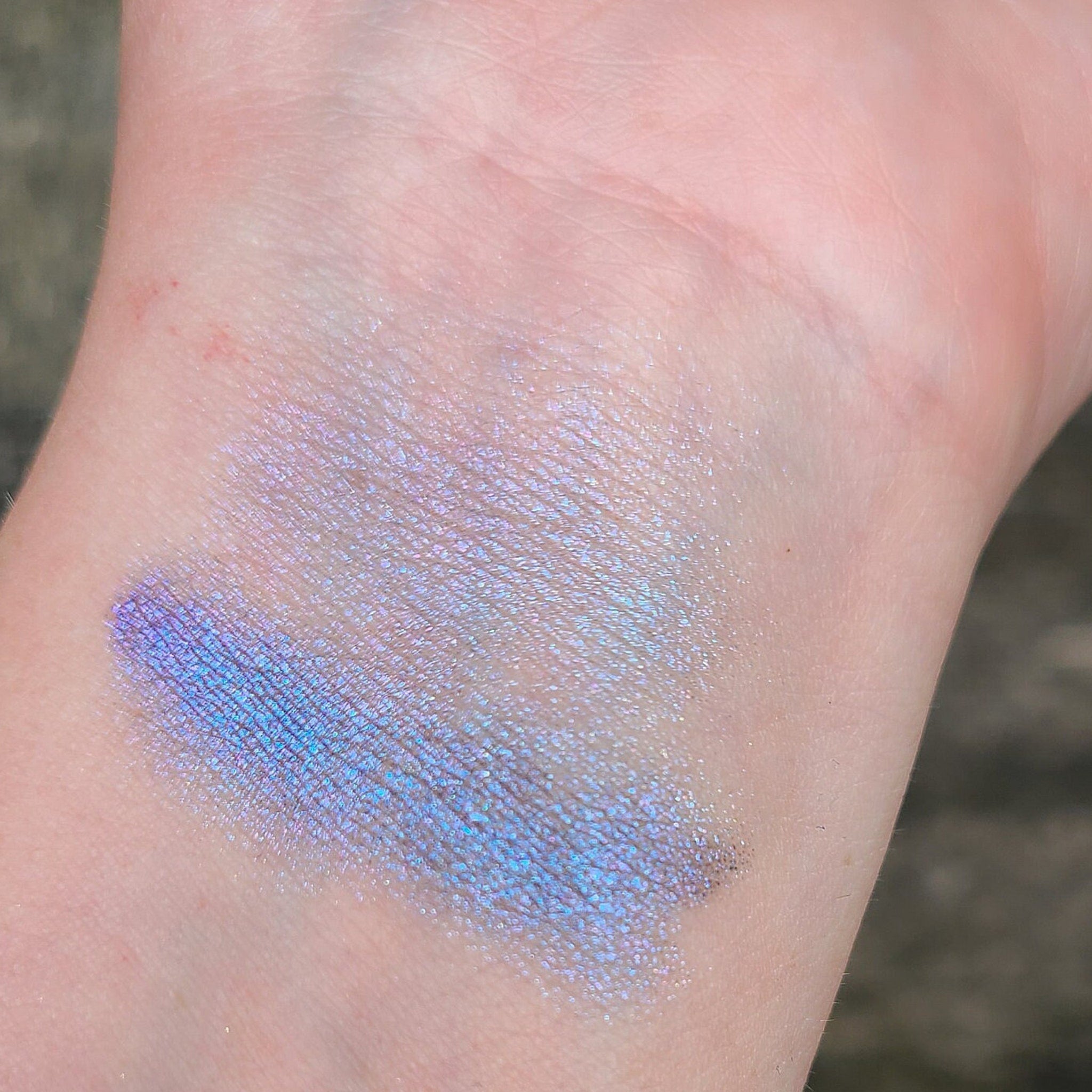 Hand applying multichrome eyeshadow with blue, purple, teal, and pink shimmer to eyelid