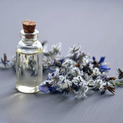 Essential oil bottle with clear glass, cork stopper, and dried blue and white flowers