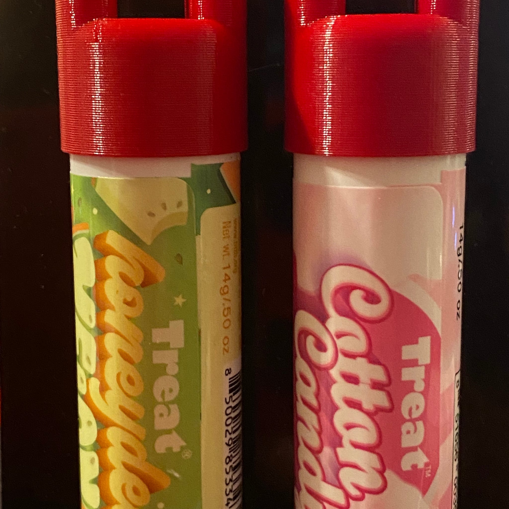 Lip balm tubes with red 3D printed lids, green and pink labels with Treat text on them