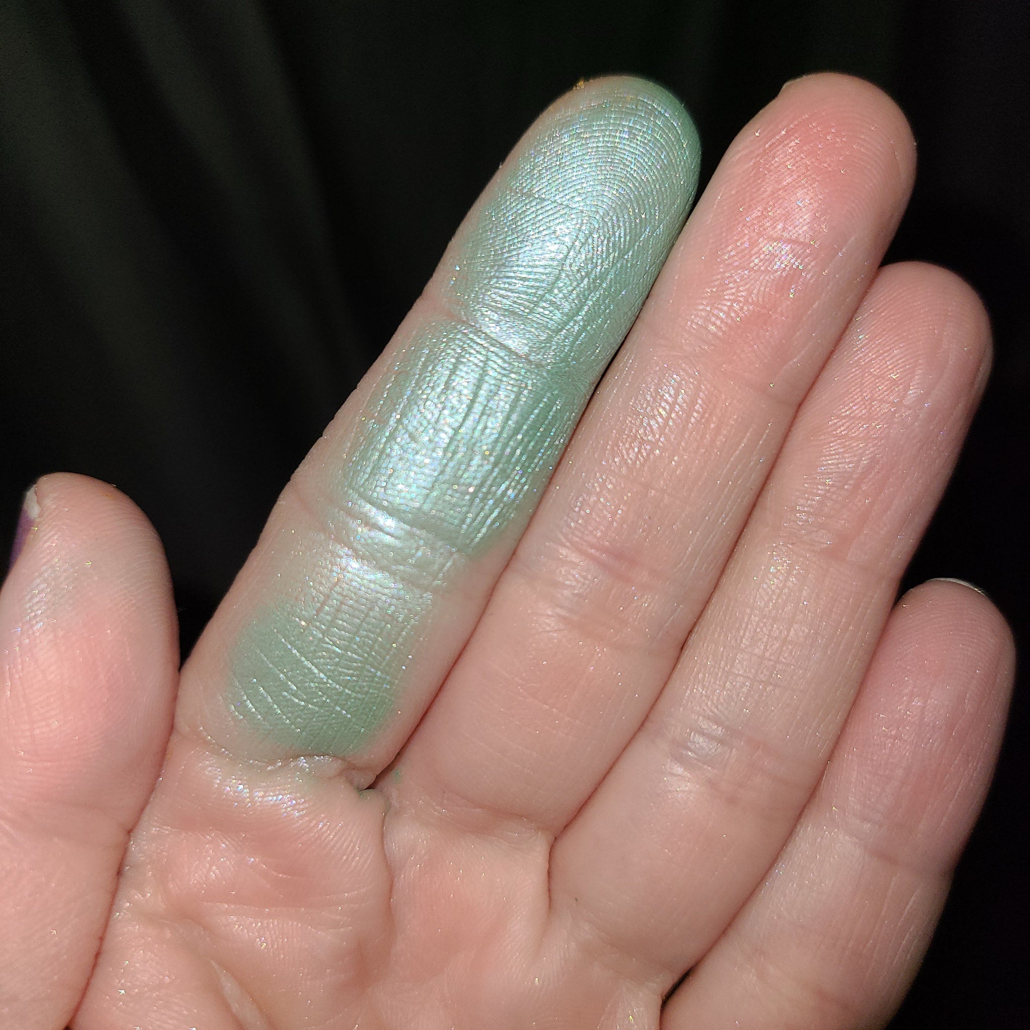 Hand applying shimmery teal and purple duochrome eyeshadow with fingertip for bold eyelid look