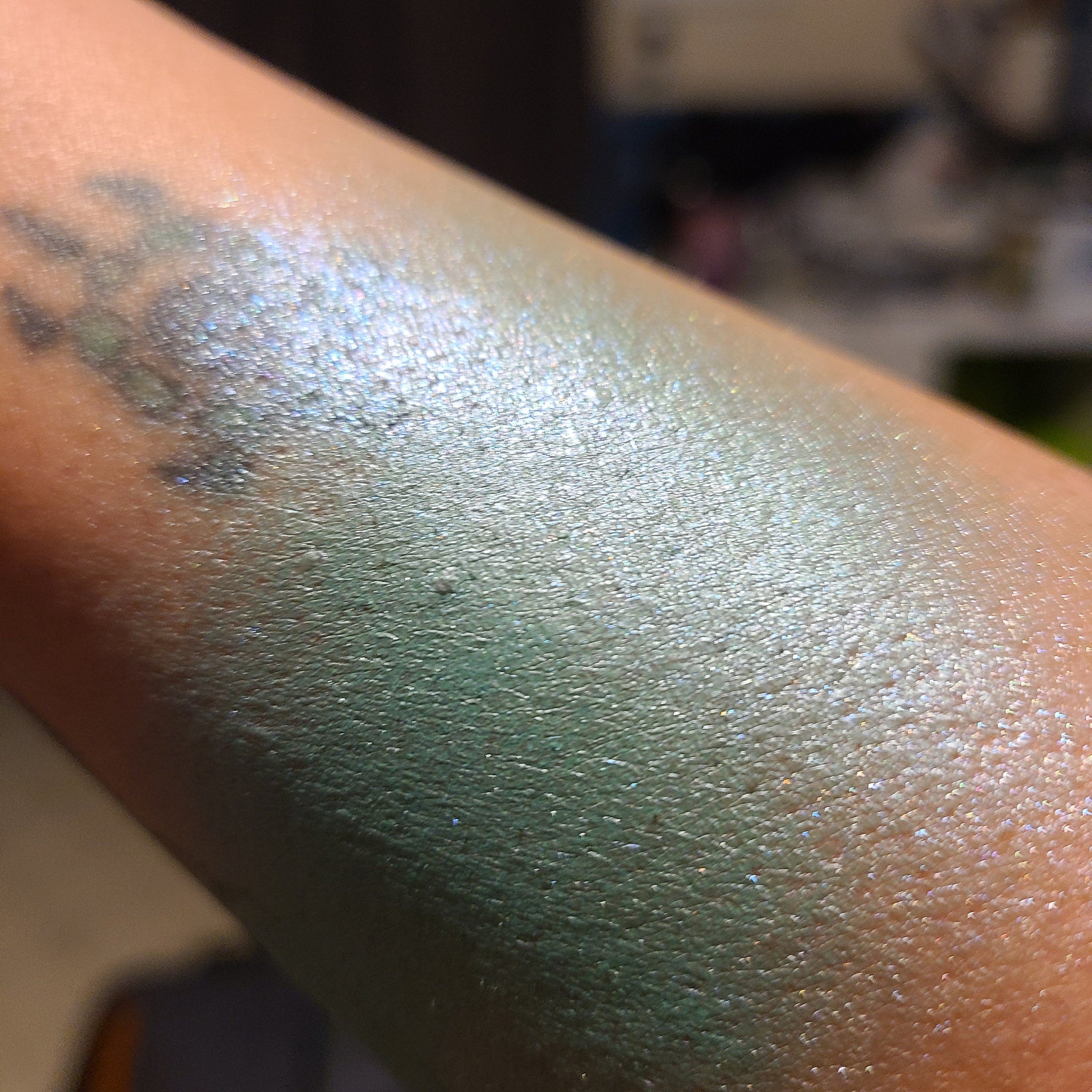 Close-up of duochrome eyeshadow pot showing vibrant blue-green shift under light