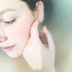 Woman's face in water, pale skin, closed eyes, hand touching ear, water around face