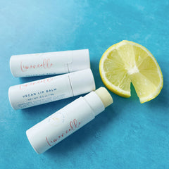 Vegan lip balm tubes in white with red text, a yellow lemon slice on blue background