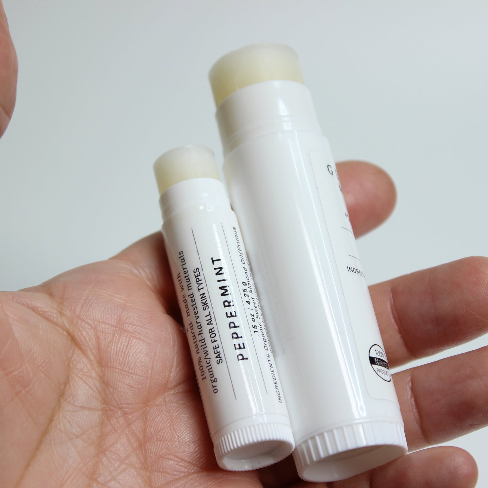Lip balm sticks, white plastic tubes with peppermint label, held in hand