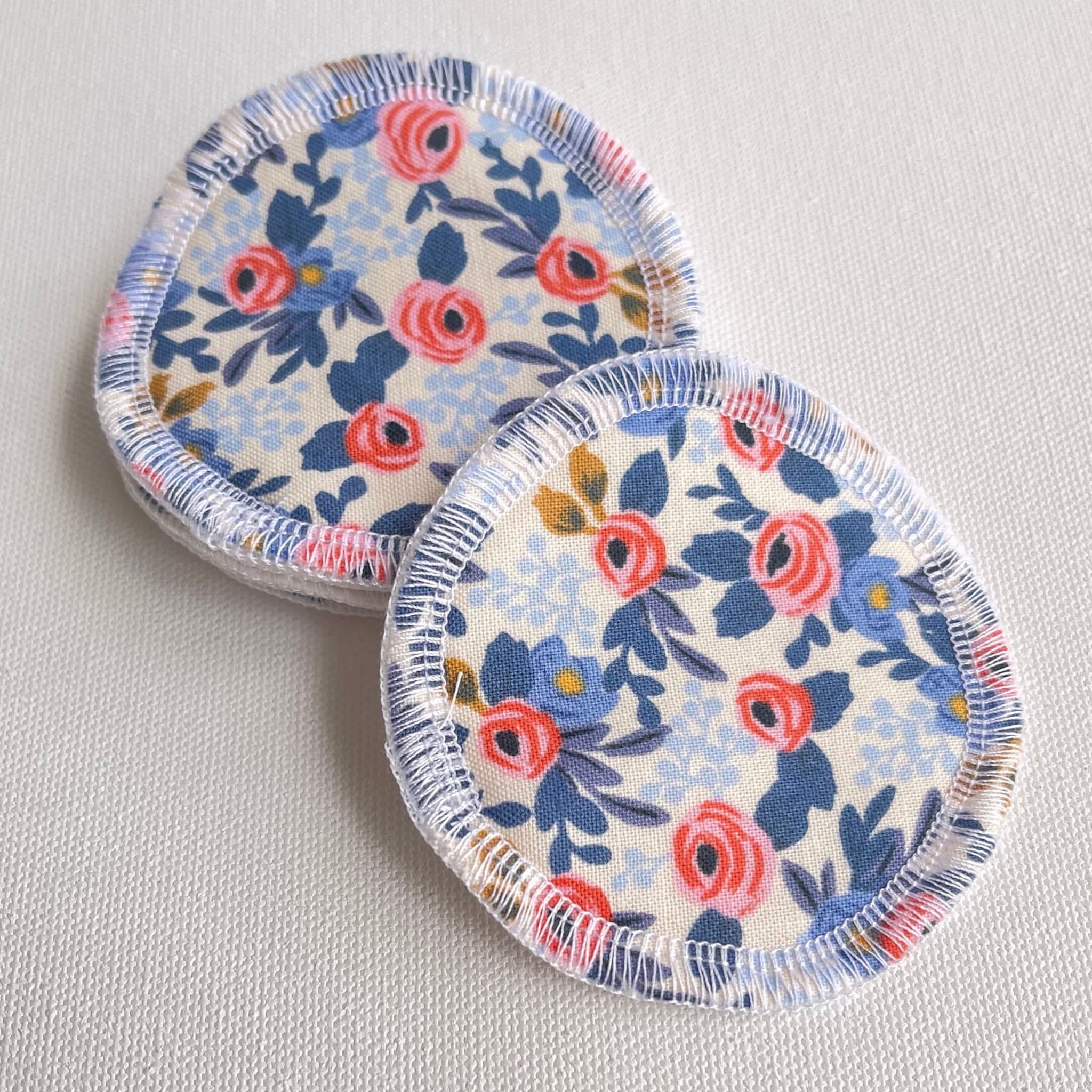 Reusable makeup remover pads with floral pattern and white stitched edges on white background