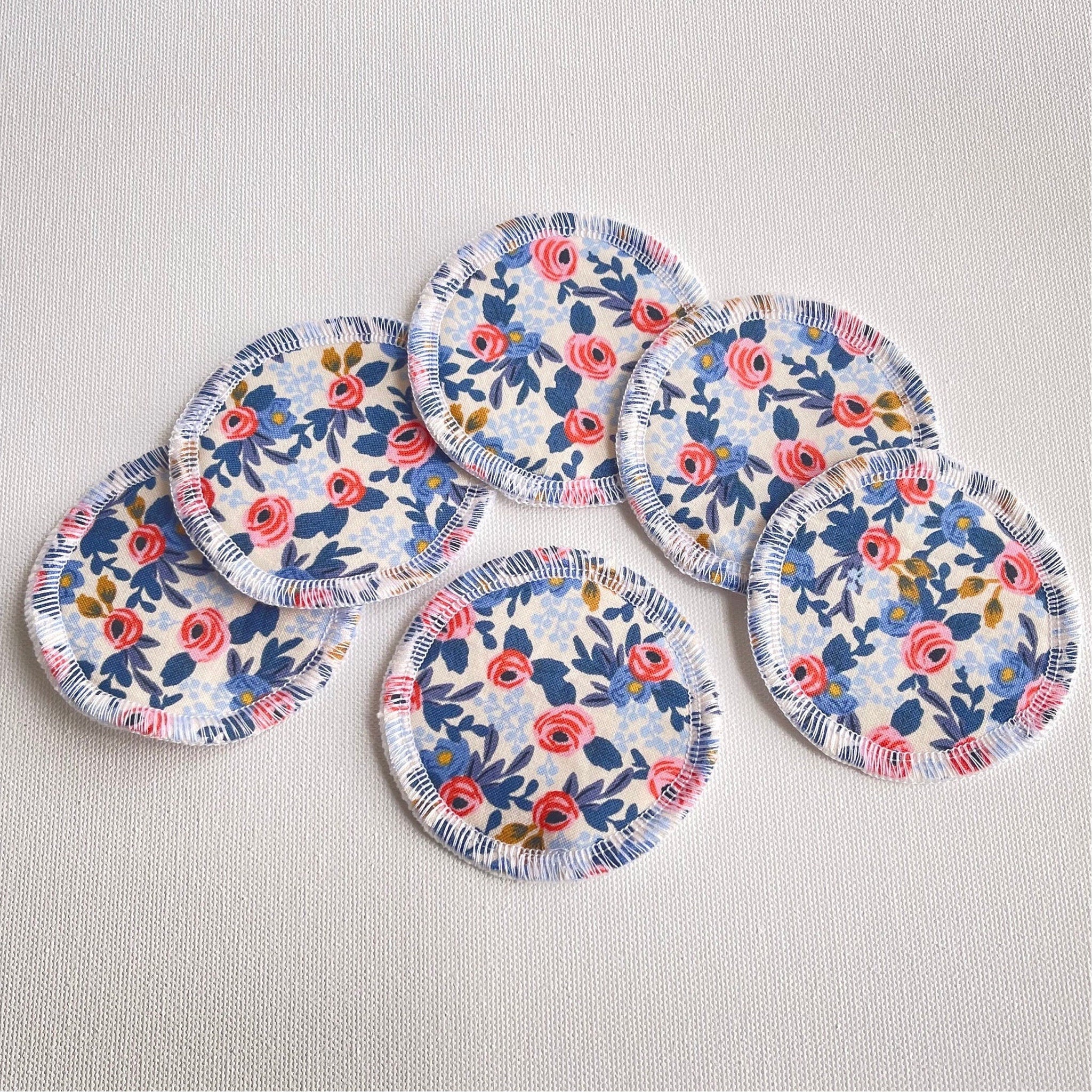 Reusable cotton pads with floral pattern, white fringe, and light fabric background