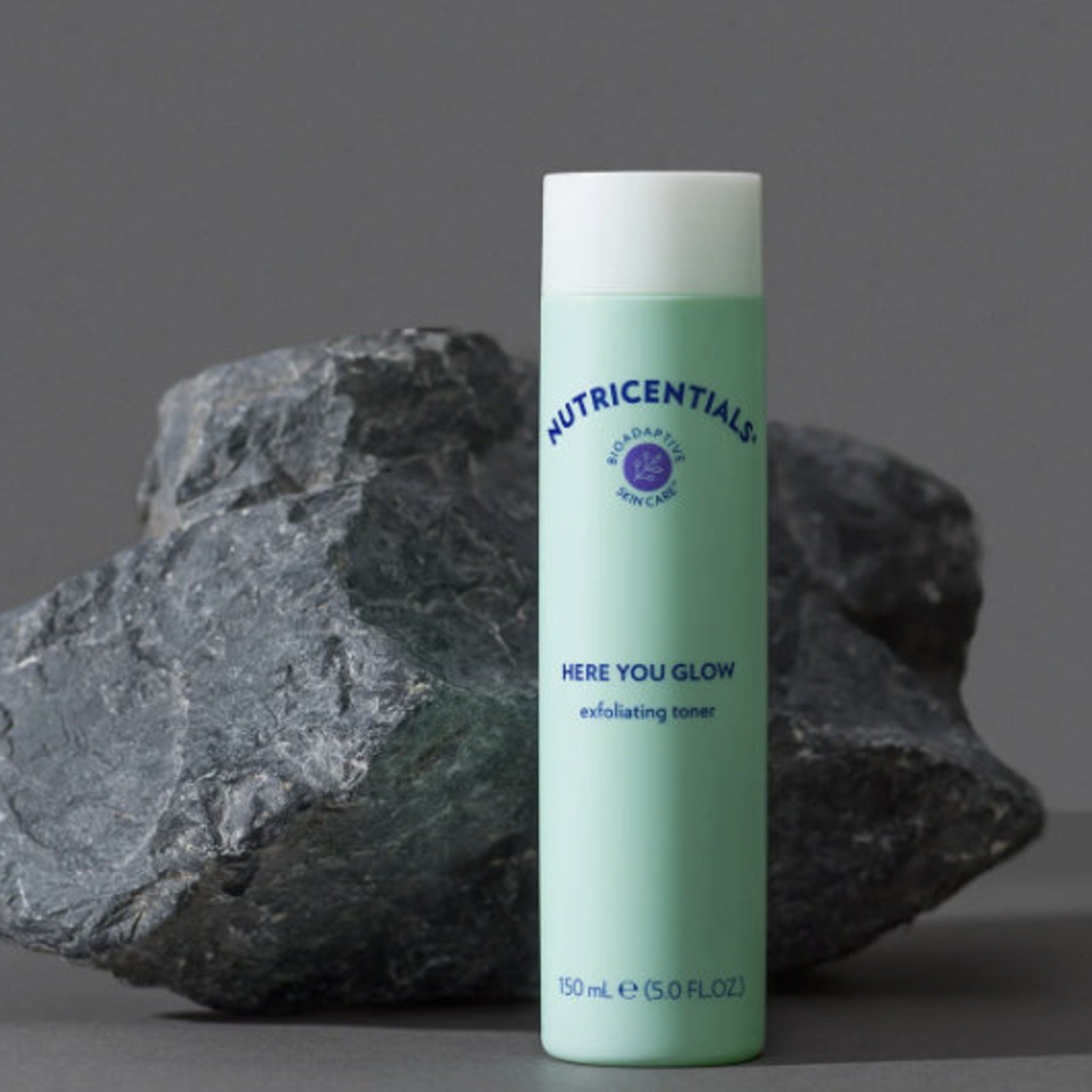 Toner bottle in green and white with Nu Skin text, set against a dark gray stone