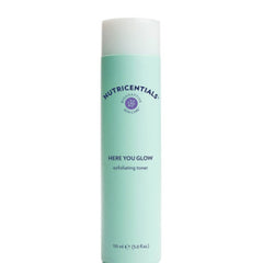 Exfoliating toner bottle in mint green, white, and purple with Nutricentials branding and Here You Glow text.