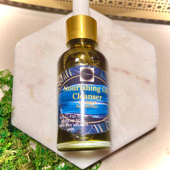 Oil cleanser bottle with gold cap, blue label, and clear liquid, on white marble surface