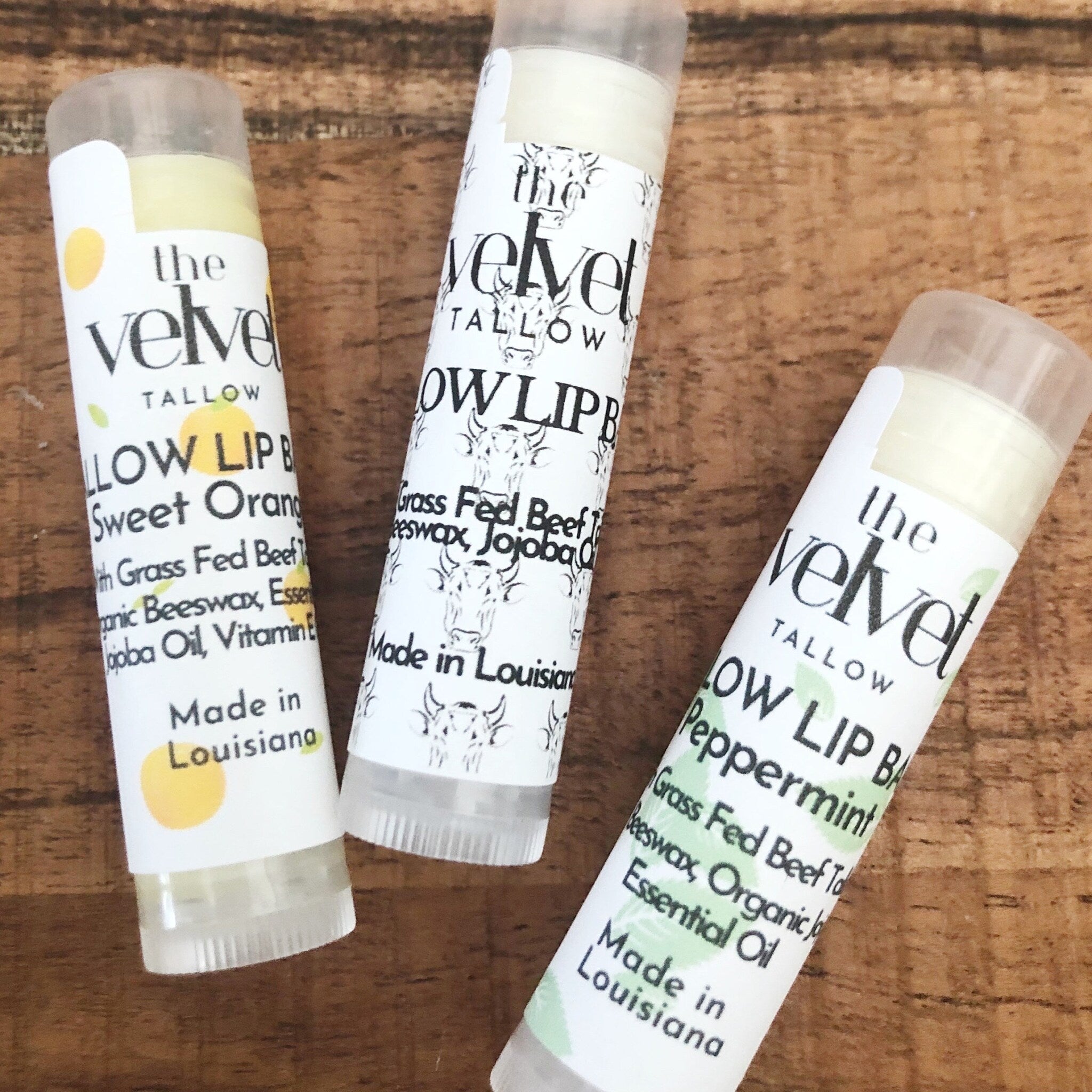 Lip balm tubes with white labels, clear caps, and "the velvet" brand text on wooden surface