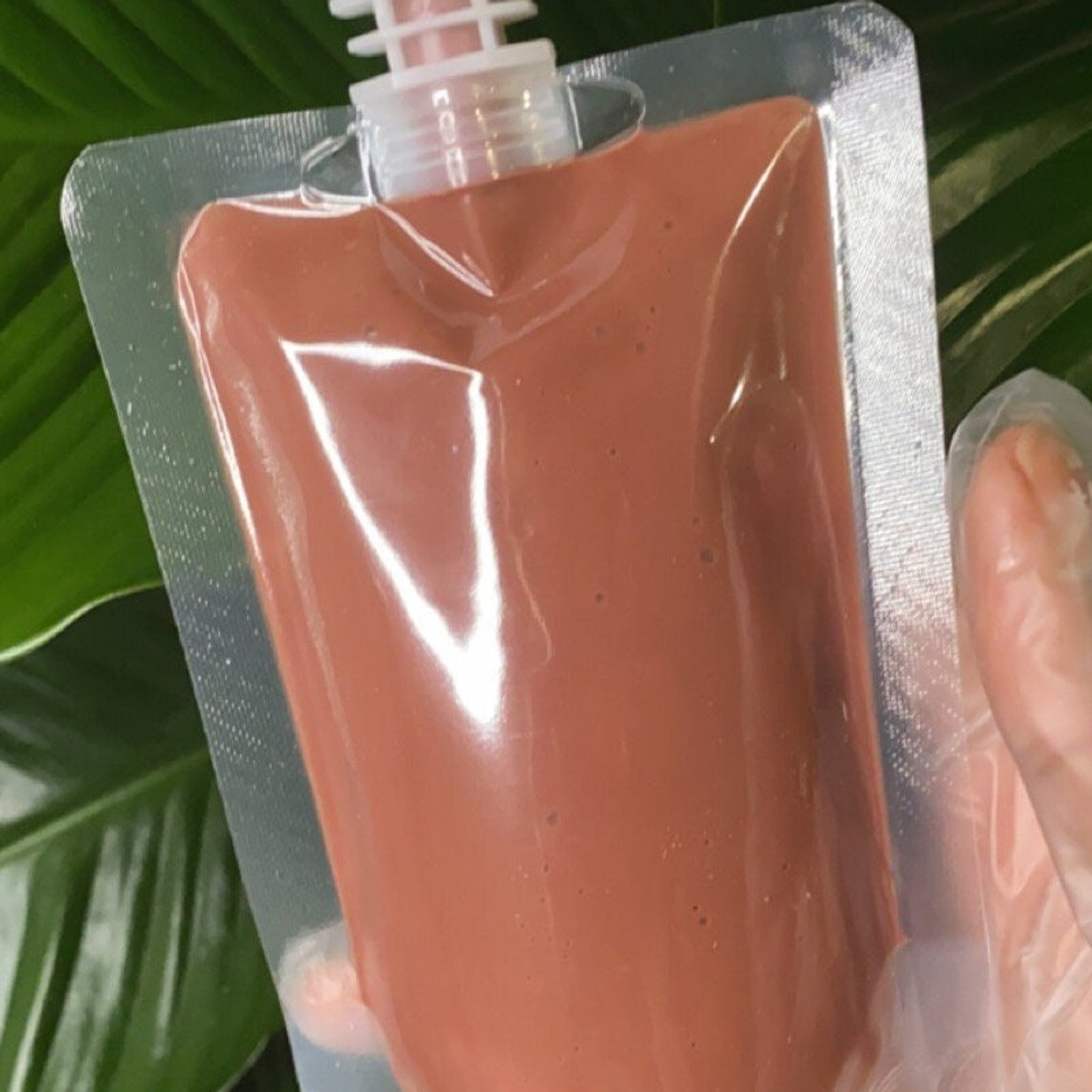 Wholesale lip gloss pouch filled with mocha-colored liquid, in a clear plastic pouch held by a gloved hand