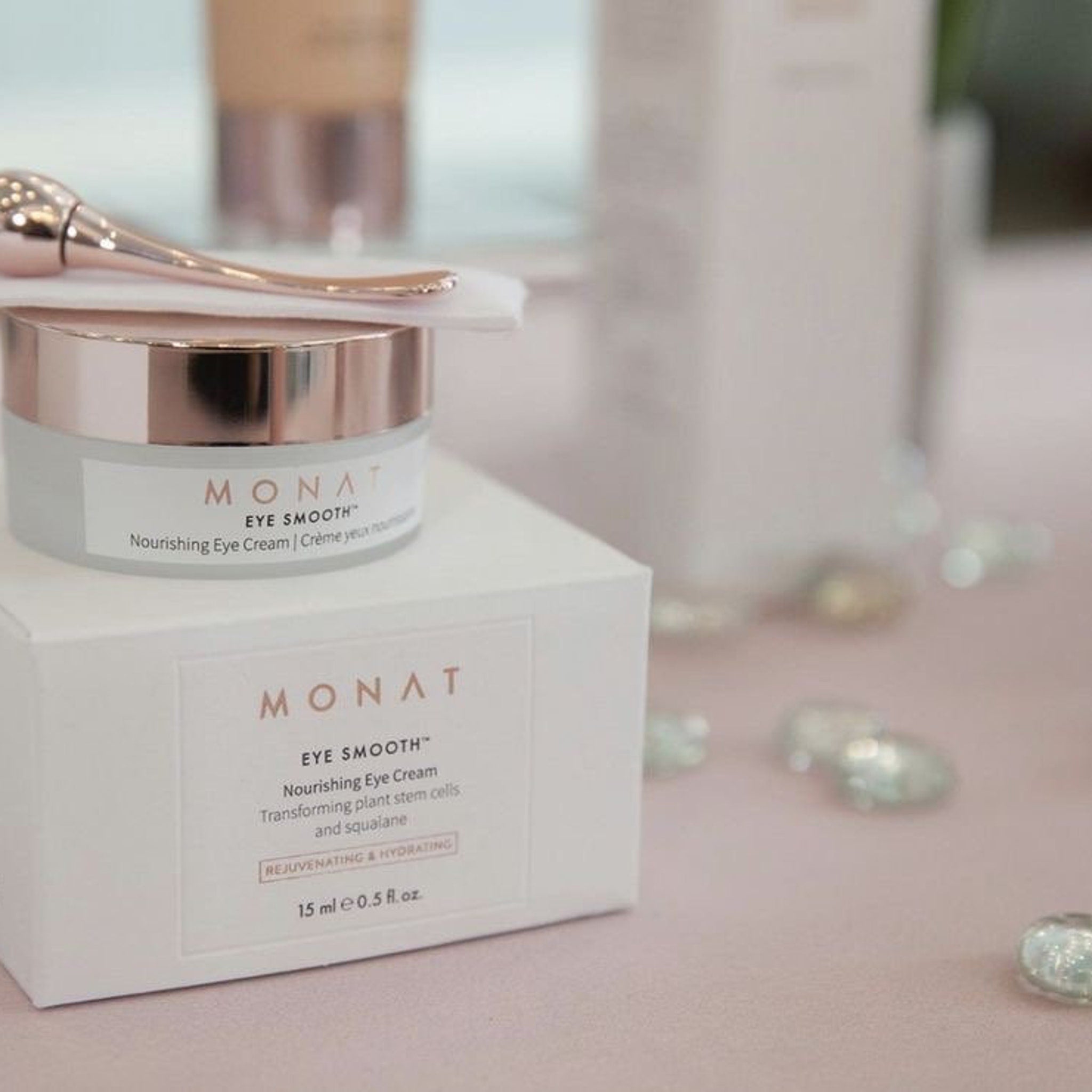 Eye cream jar with rose gold lid and white label, on white box with MONAT branding, eye cream applicator visible