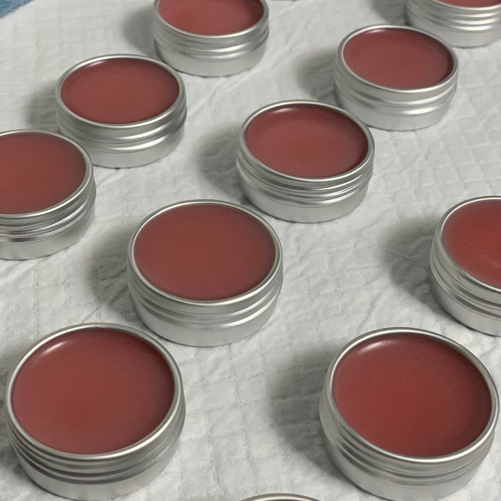 Lip balm in red color, contained in silver metal tins, arranged on white surface