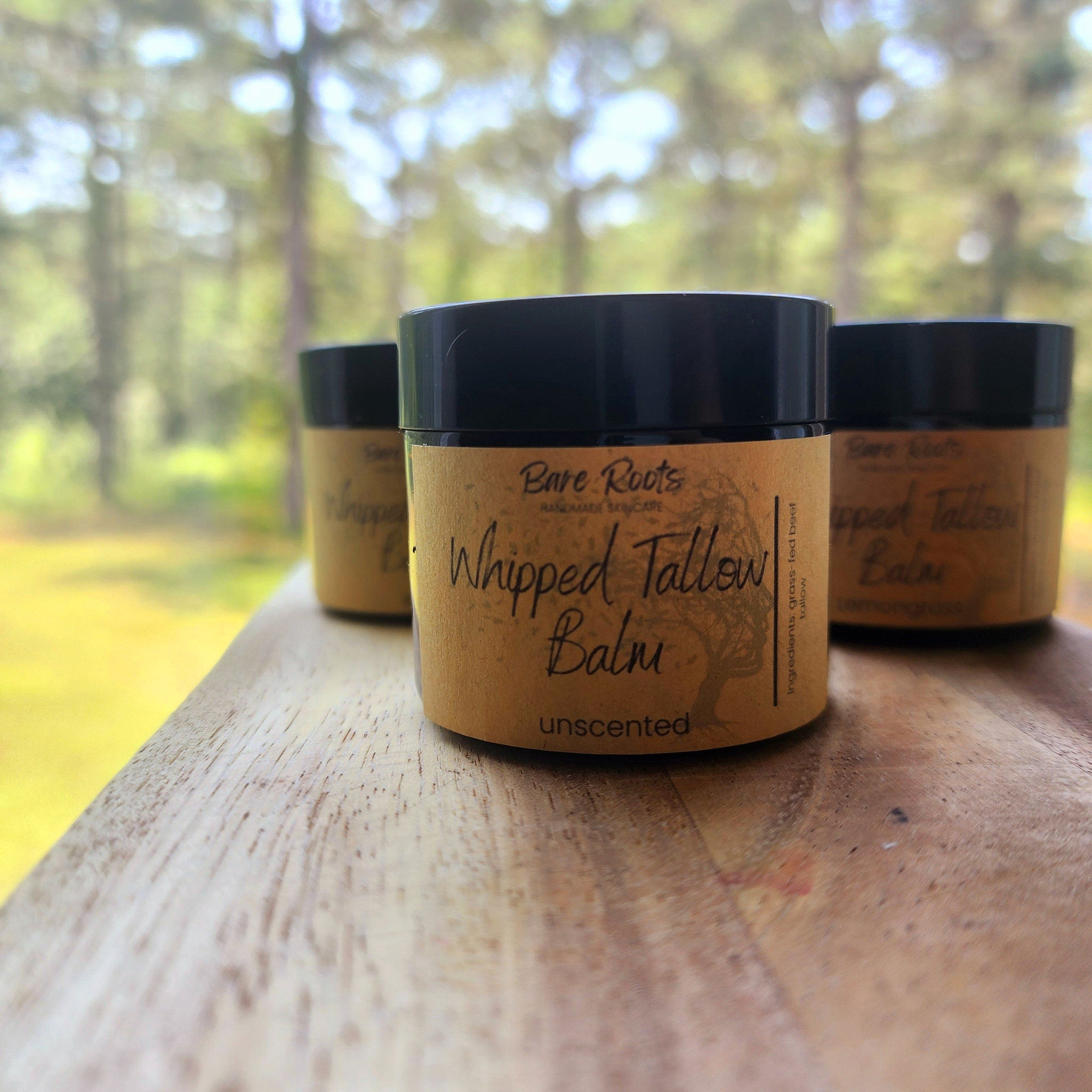 Side view of golden whipped tallow balm in glass jar with minimalist black lid on marble surface