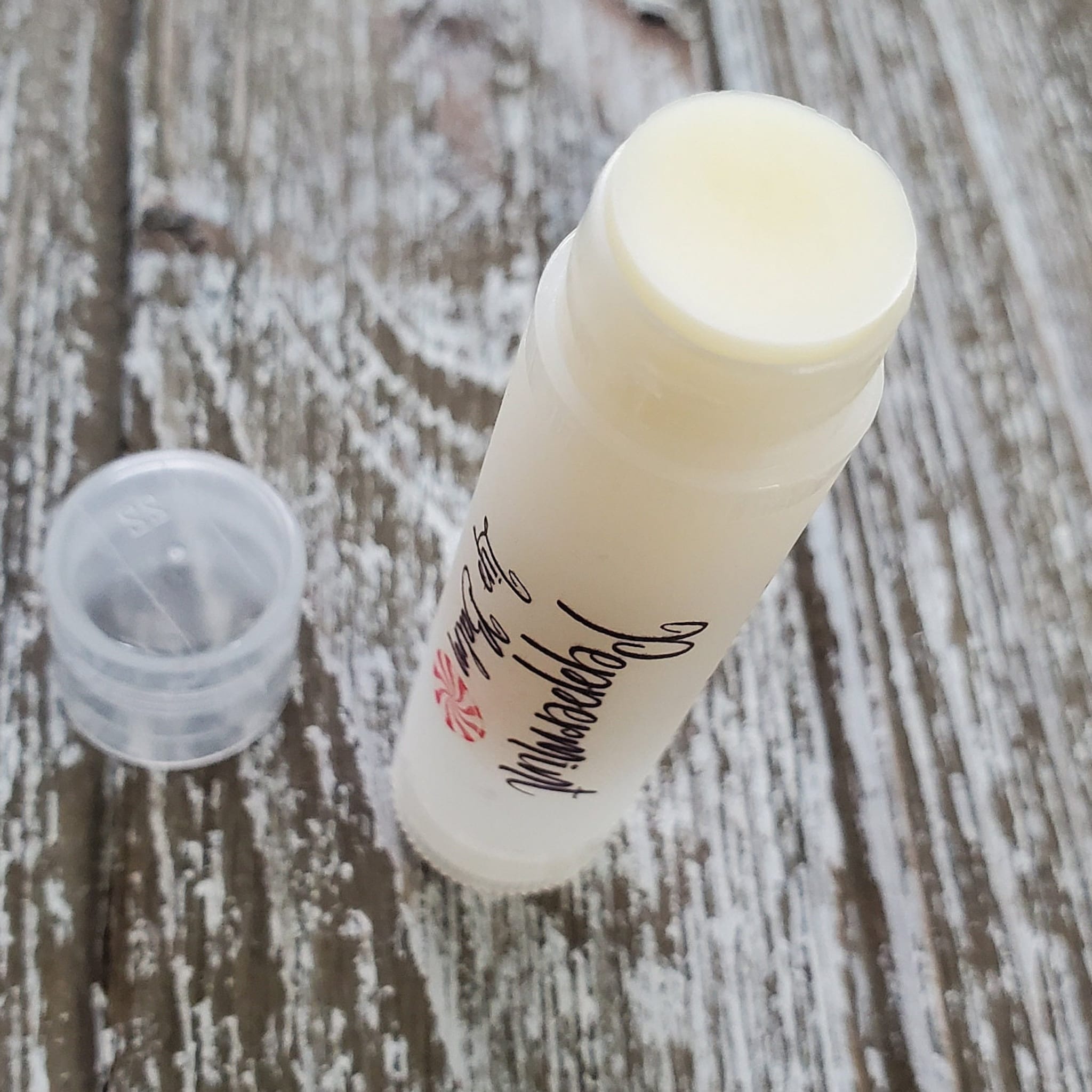 Lip balm tube with white and clear plastic, visible "Peppermint" text, and wooden background