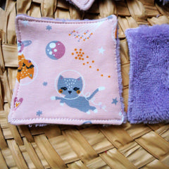 Pink patterned square fabric with cat print and purple fluffy fabric on woven surface