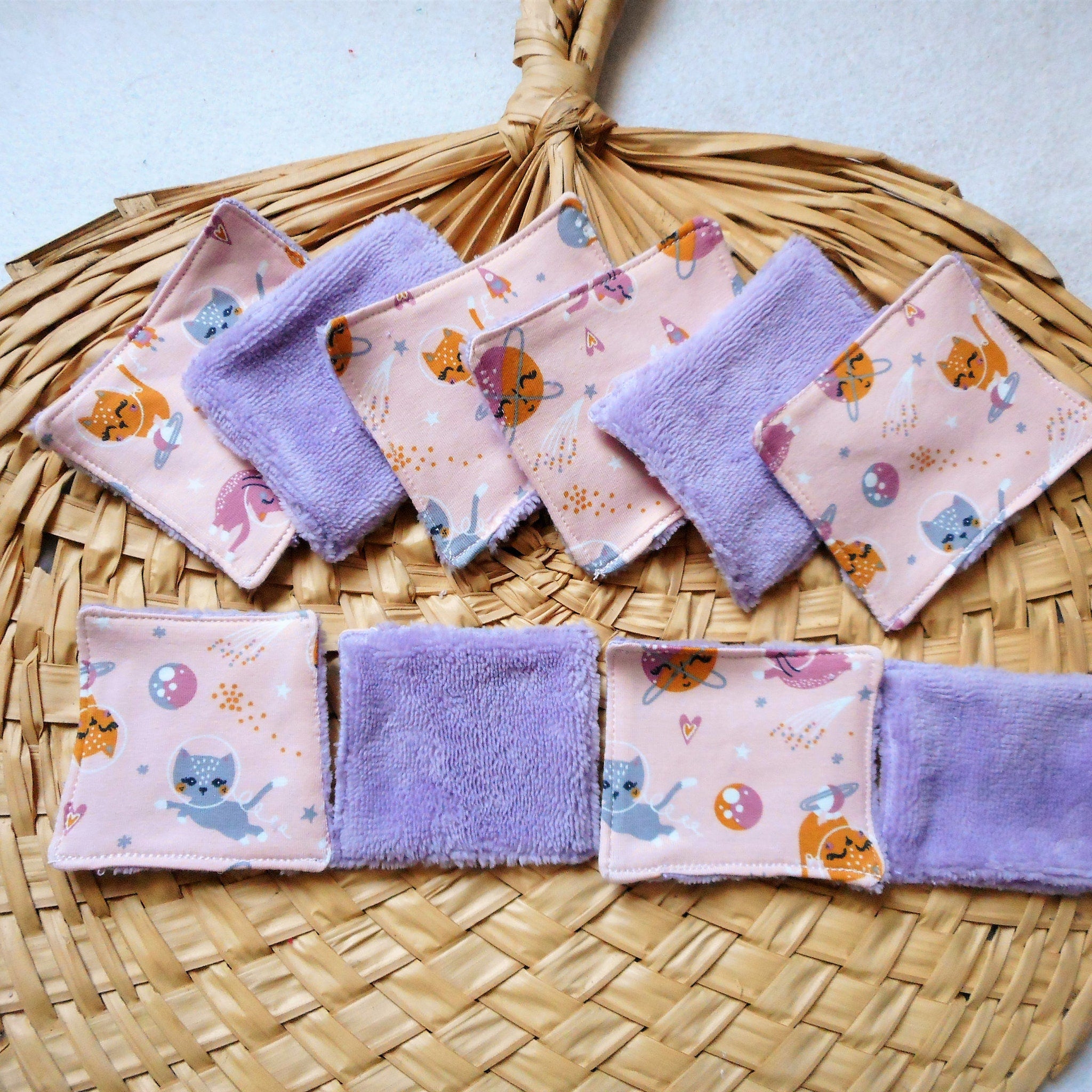 Reusable face pads with pink cat print and purple plush material on woven basket