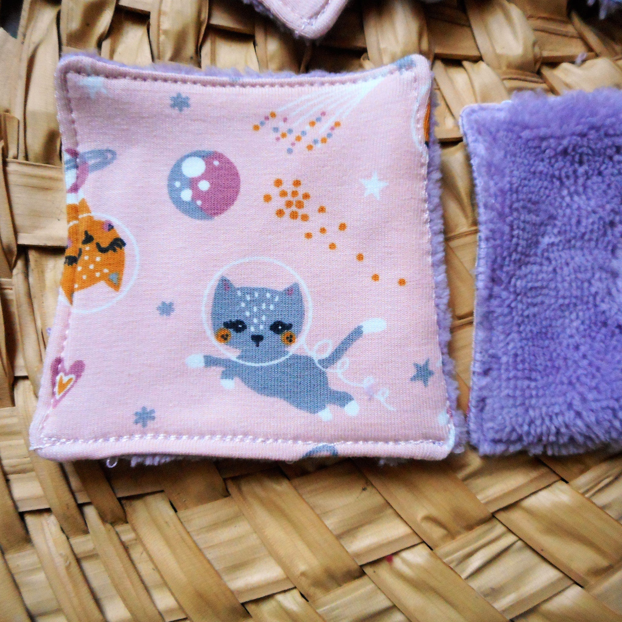 Reusable face pads with pink cat pattern and purple fluffy pad on woven surface