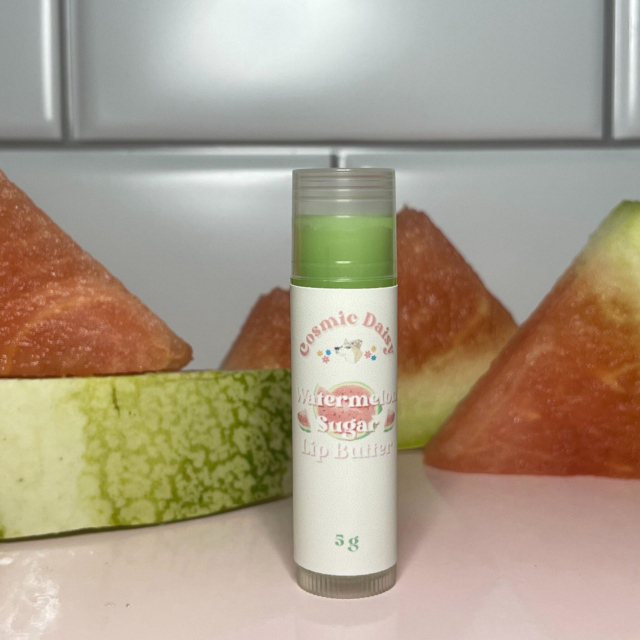Lip butter tube with green balm, white label, and watermelon slices in background