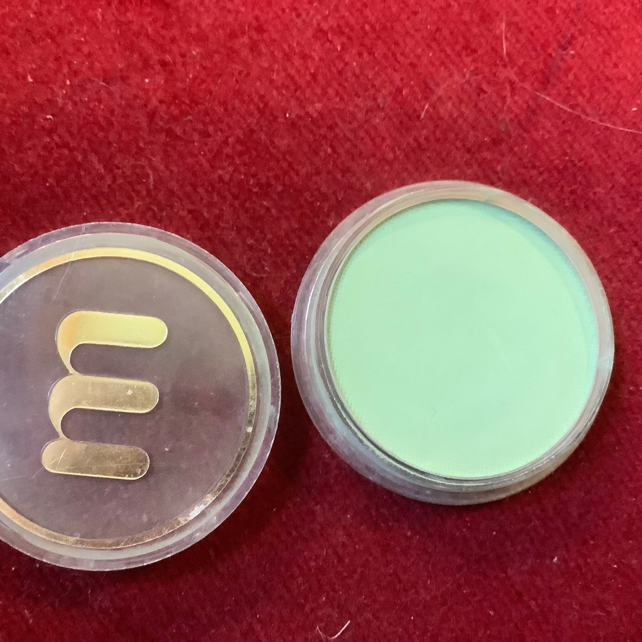 Green powder compact with clear lid and gold trim on red background