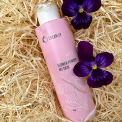Face powder product in pink bottle with floral design, purple flowers, and straw background